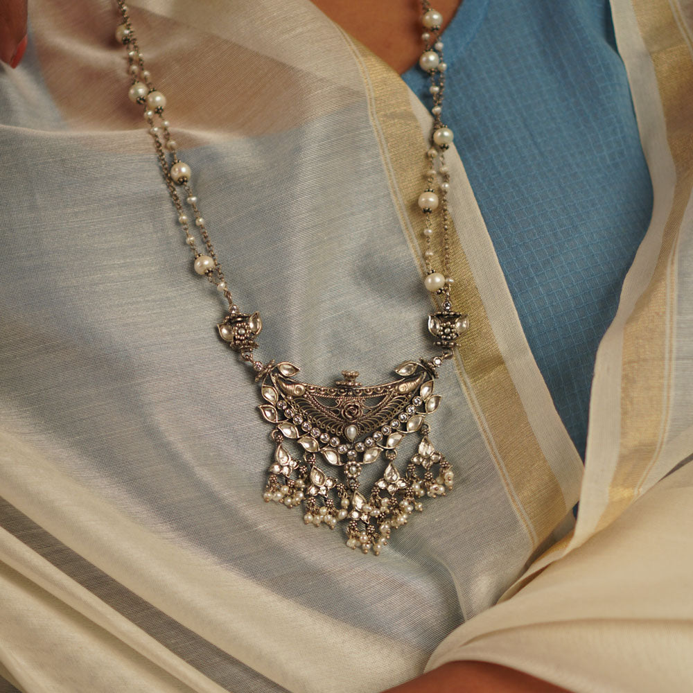 This oxidized silver necklace, adorned with luminous white kundan stones and delicate pearls, exudes an air of vintage sophistication. A perfect harmony of tradition and elegance, it’s a timeless statement piece.