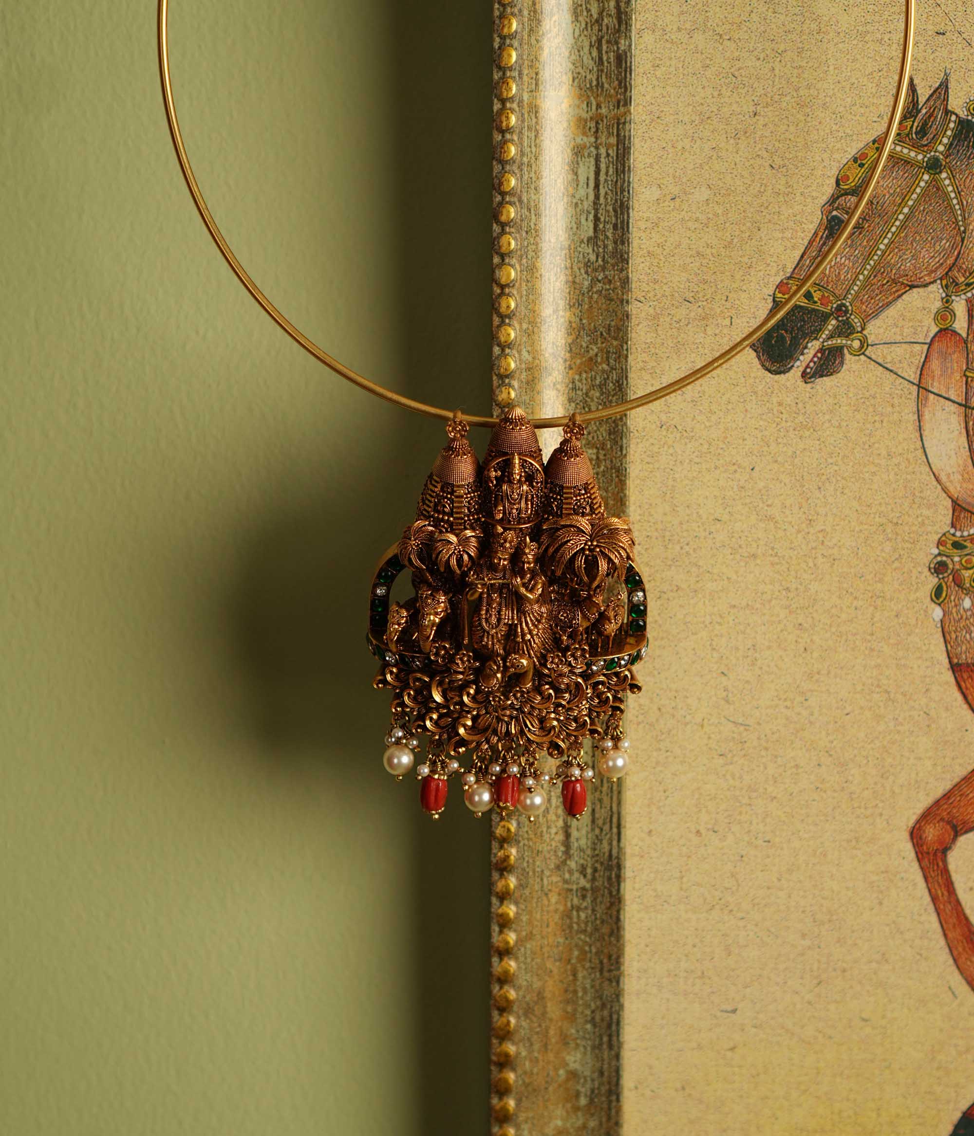 Exquisite gold-plated silver temple jewelry pendant featuring a divine depiction of Lord Krishna and Radha, surrounded by intricate carvings of animals and nature. Adorned with radiant white and green Kundan stones, vibrant red coral beads, and delicate freshwater pearls, this pendant offers both single and double hooks for versatile styling, making it a perfect blend of spirituality and elegance.