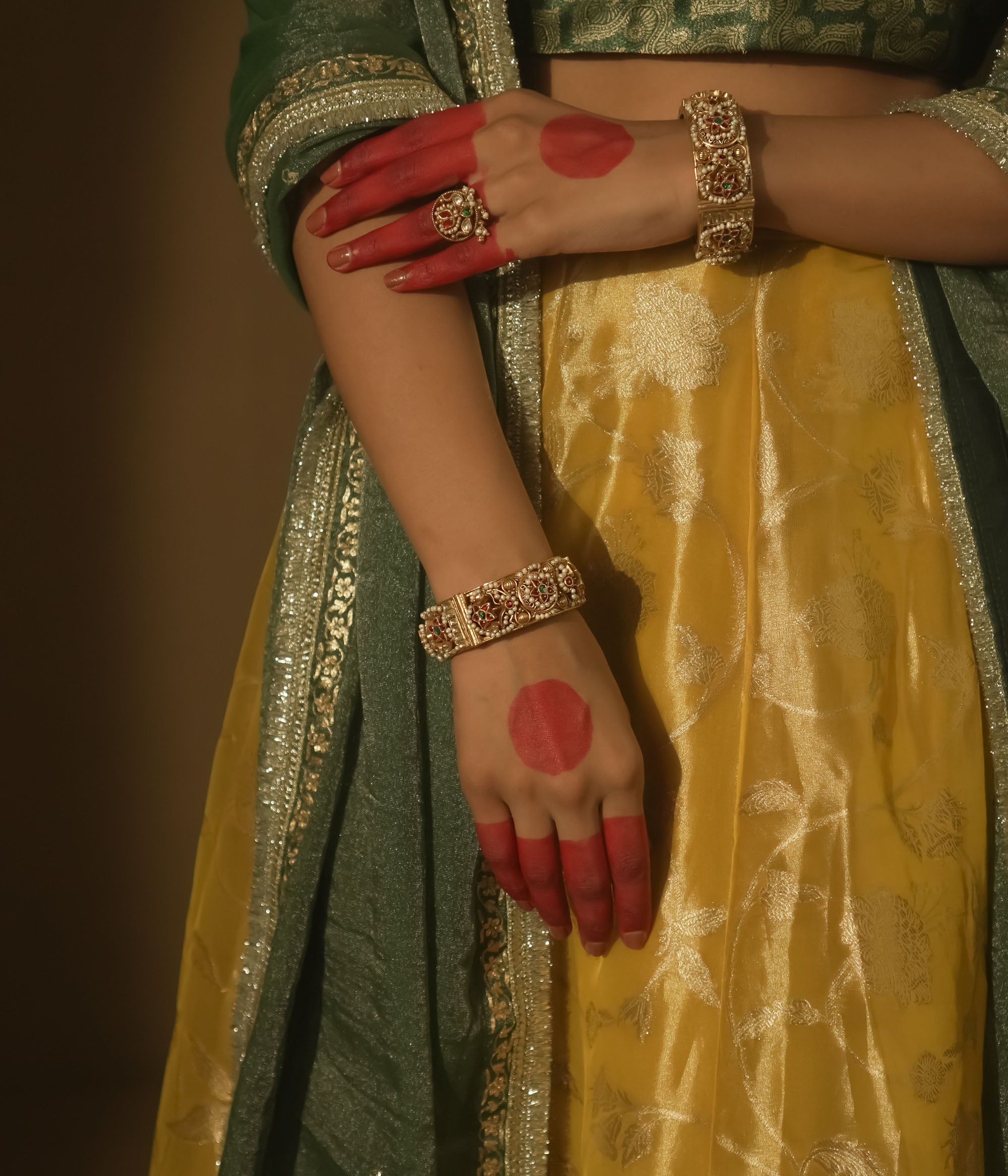 Gold-plated bangle with red and green Kundan gems and intricate patterns.