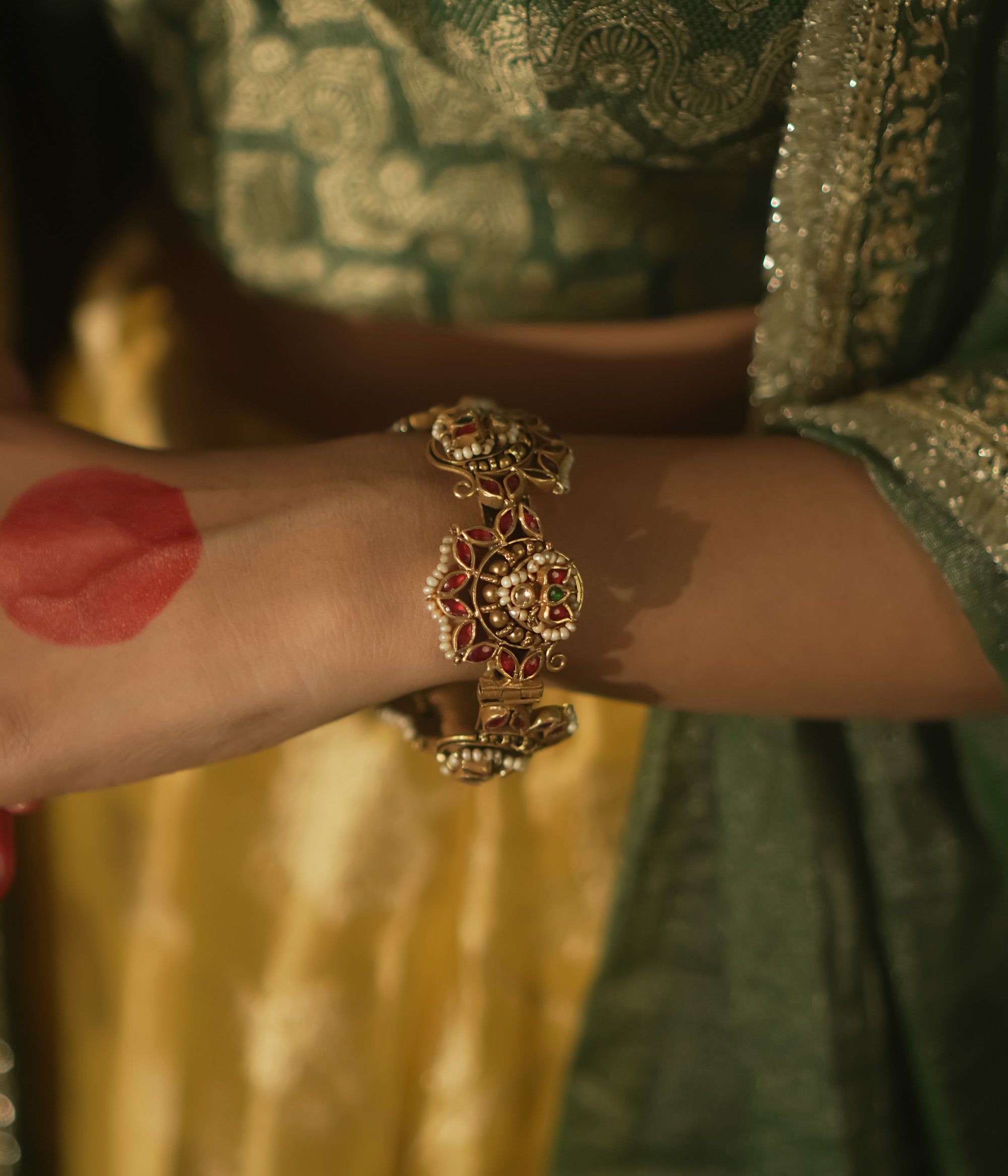 Gold-plated silver bangle with filigree, red Kundan gems, and pearls.