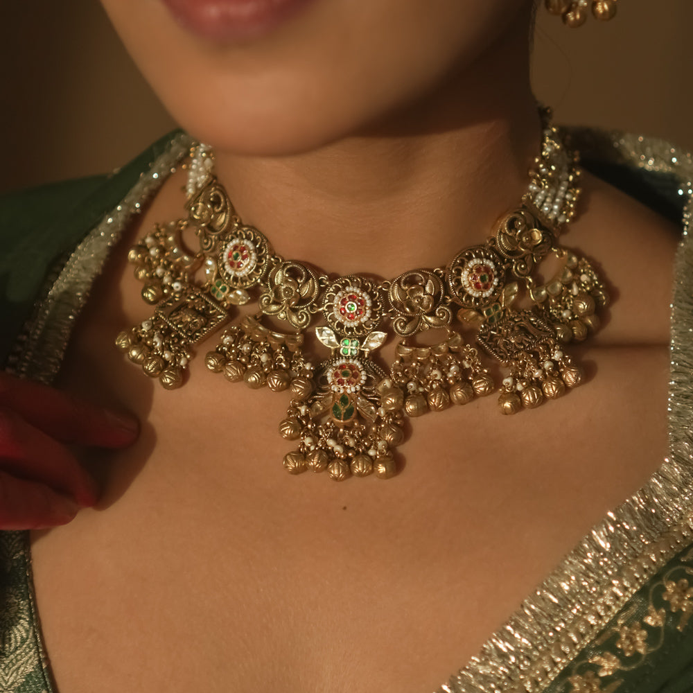 Gold-plated necklace with intricate swirls, red, green, and white gems, pearls, and bells.