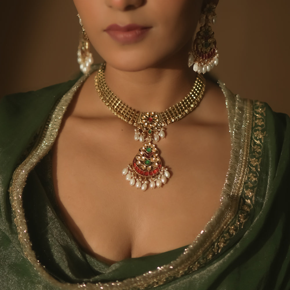 Gold necklace with a central pendant, rubies, emeralds, and dangling pearls.