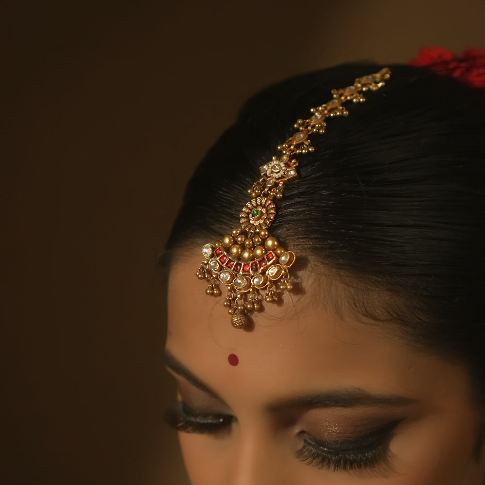 Gold-plated silver maangtika with red, green, and clear Kundan stones and tiny bells.