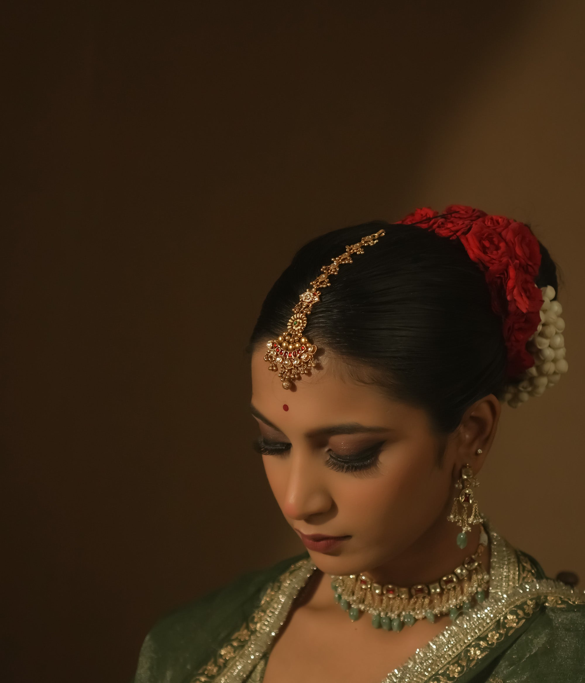 Gold-plated silver maangtika with red, green, and clear Kundan stones and tiny bells.