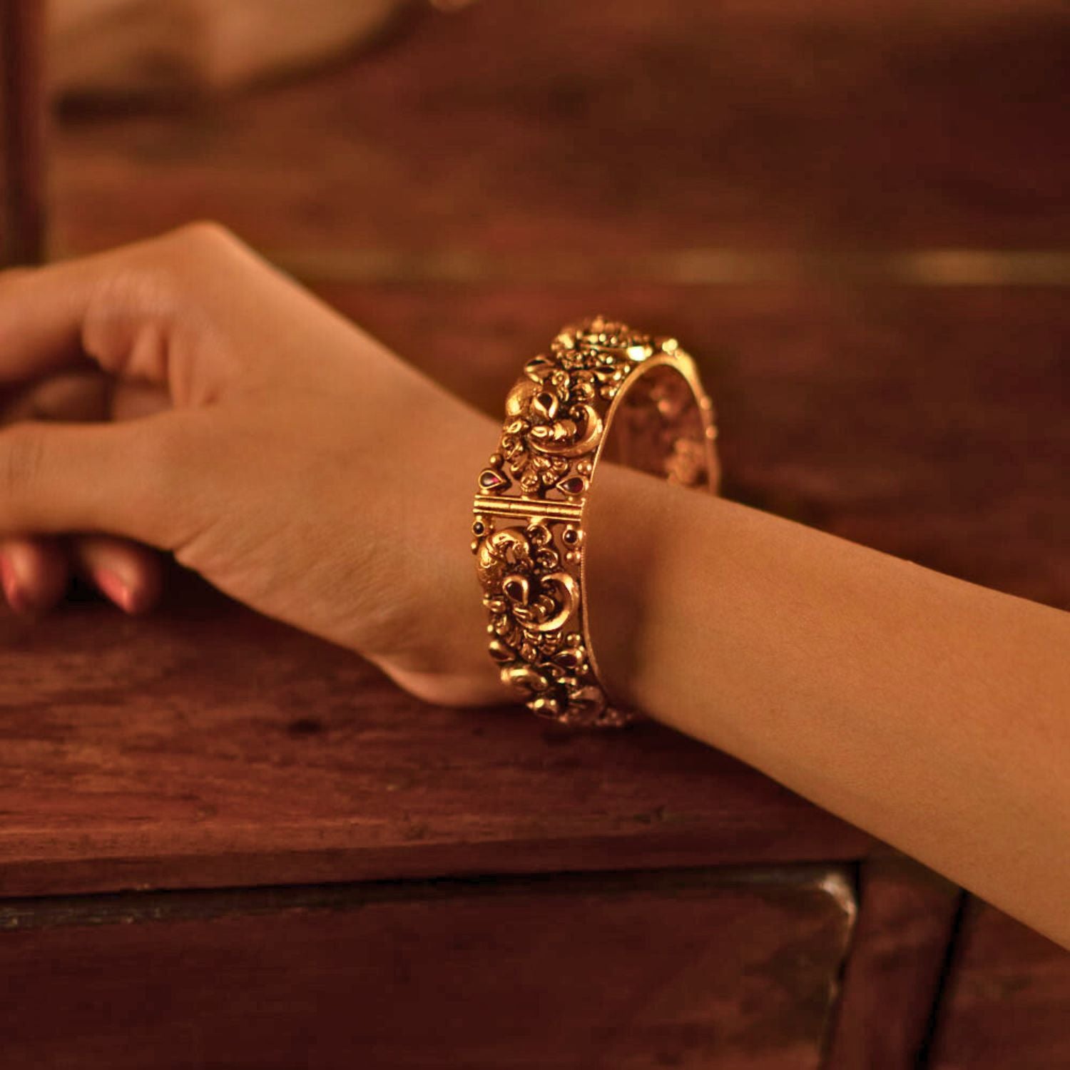 The Jagvi Kada, meticulously handcrafted in antique gold-plated silver, showcases exquisite temple-inspired details with pink kundans set in a classic kaairi pattern, reflecting timeless heritage and craftsmanship.