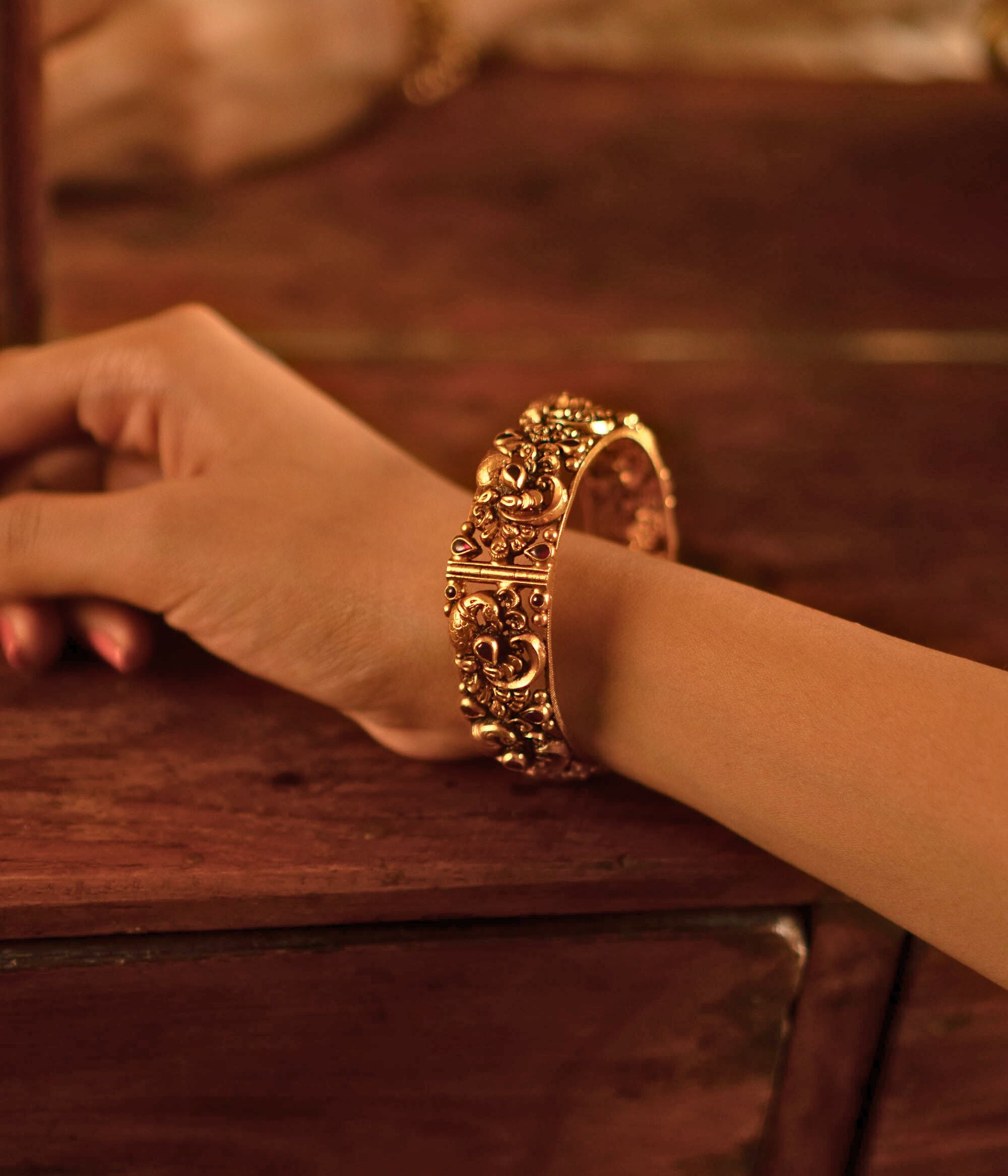 The Jagvi Kada, meticulously handcrafted in antique gold-plated silver, showcases exquisite temple-inspired details with pink kundans set in a classic kaairi pattern, reflecting timeless heritage and craftsmanship.