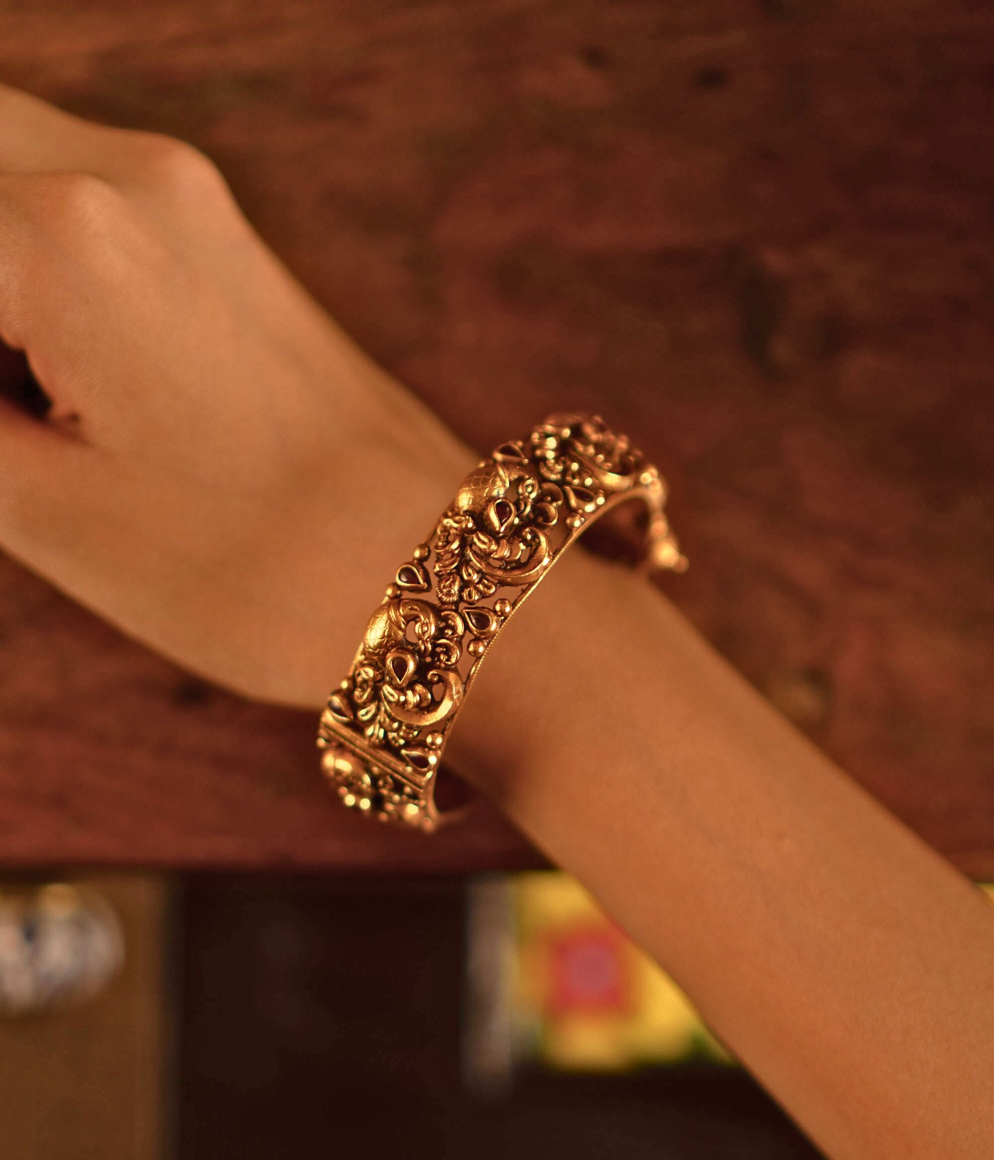 The Jagvi Kada, meticulously handcrafted in antique gold-plated silver, showcases exquisite temple-inspired details with pink kundans set in a classic kaairi pattern, reflecting timeless heritage and craftsmanship.