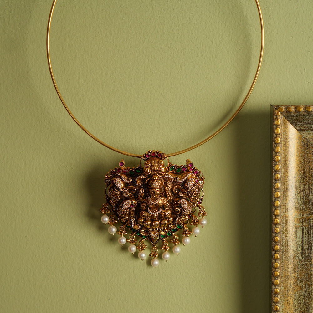 Traditional gold-plated silver temple jewelry pendant featuring Goddess Lakshmi at the center, adorned with radiant red and green Kundan stones and elegant pearl drops. Designed with both single and double hooks for versatile styling, this pendant exudes divine grace and timeless craftsmanship.