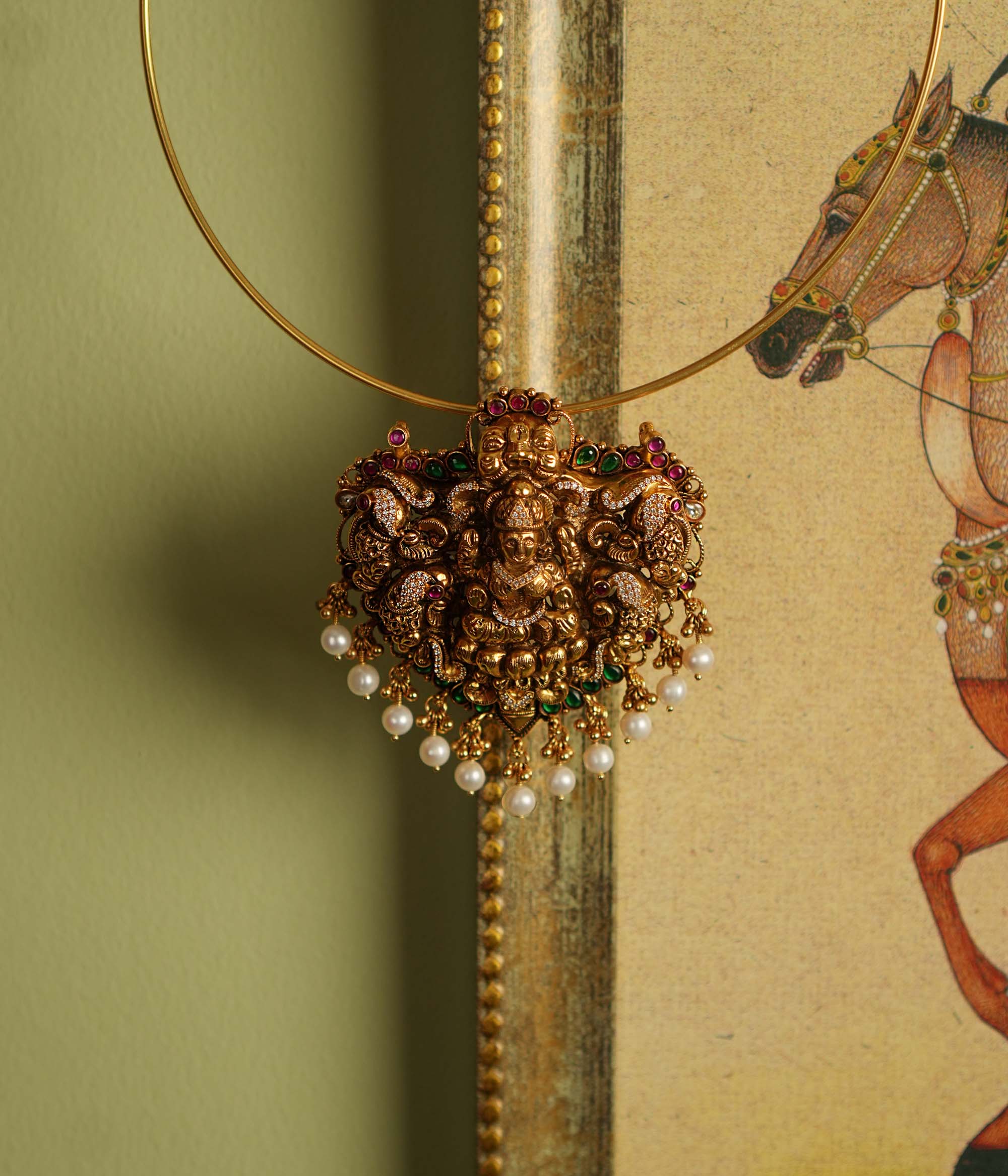 Traditional gold-plated silver temple jewelry pendant featuring Goddess Lakshmi at the center, adorned with radiant red and green Kundan stones and elegant pearl drops. Designed with both single and double hooks for versatile styling, this pendant exudes divine grace and timeless craftsmanship.