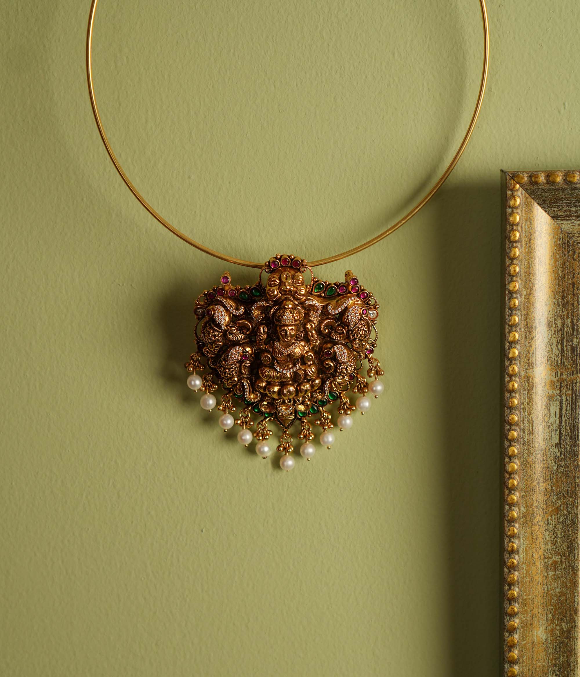 Traditional gold-plated silver temple jewelry pendant featuring Goddess Lakshmi at the center, adorned with radiant red and green Kundan stones and elegant pearl drops. Designed with both single and double hooks for versatile styling, this pendant exudes divine grace and timeless craftsmanship.