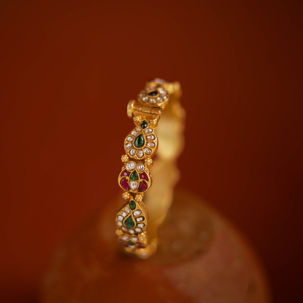 Gold bangle with red, green, and white kundan stones in traditional floral design.