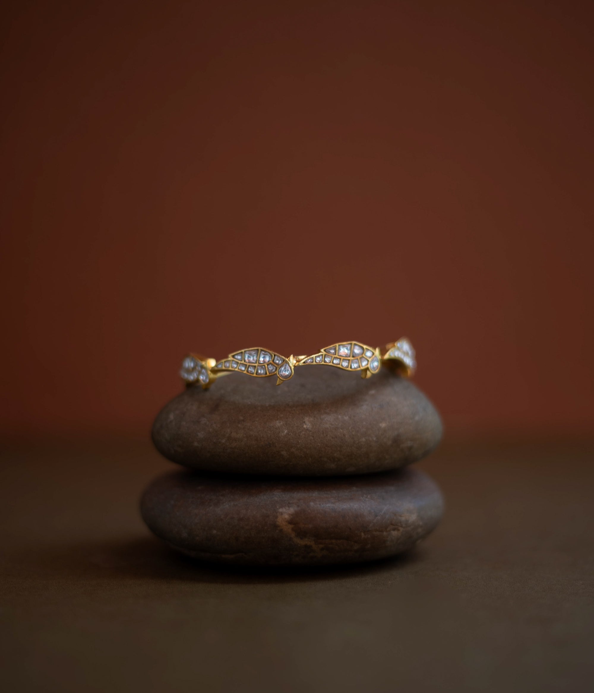 Close-up of a delicate gold bangle. Small, sparkling stones are set in a repeating, wave-like pattern along its circumference.