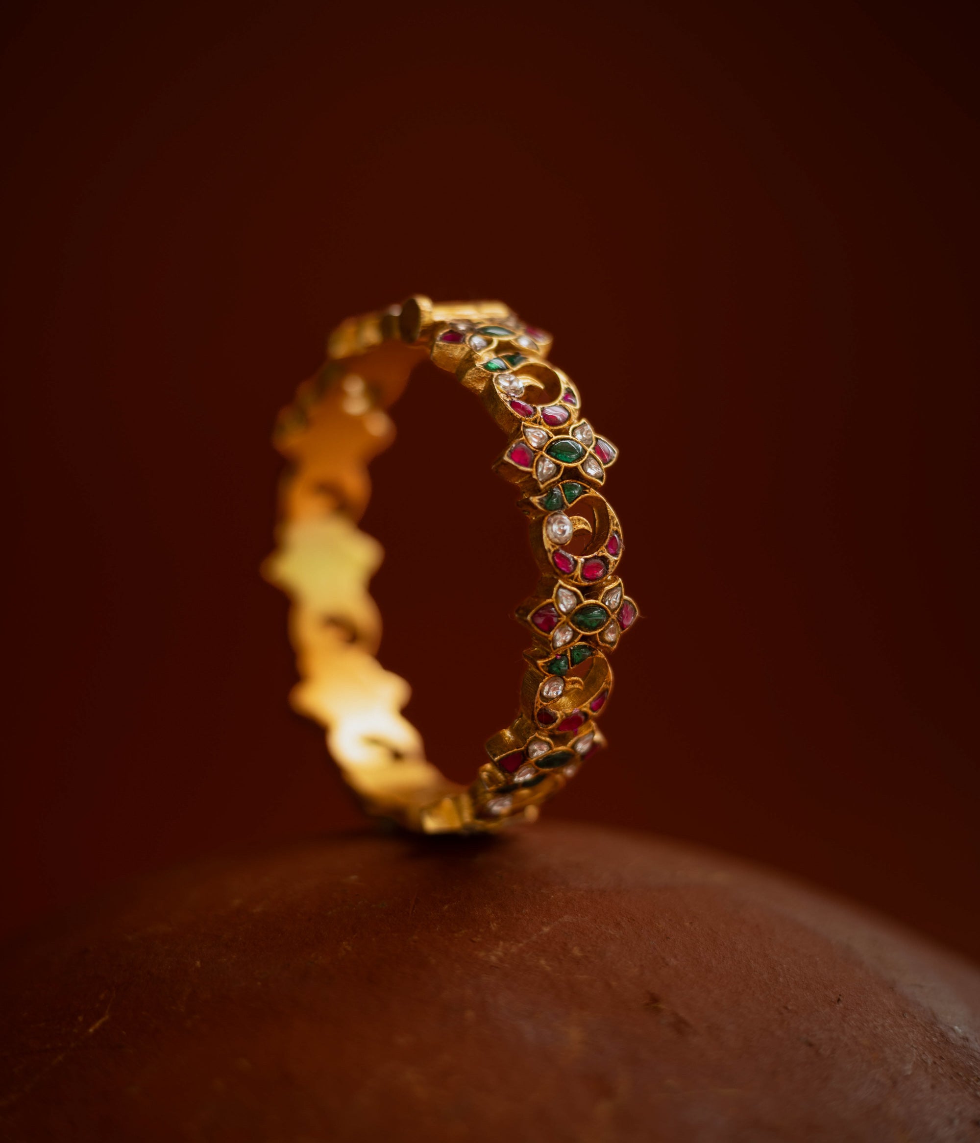 Kundan bangle with alternating moon and floral motifs, set in red, green, white stones.