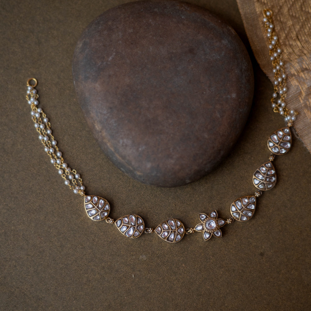 Gold choker with white kundan leaf motifs, floral centerpiece, and pearl chain detailing.