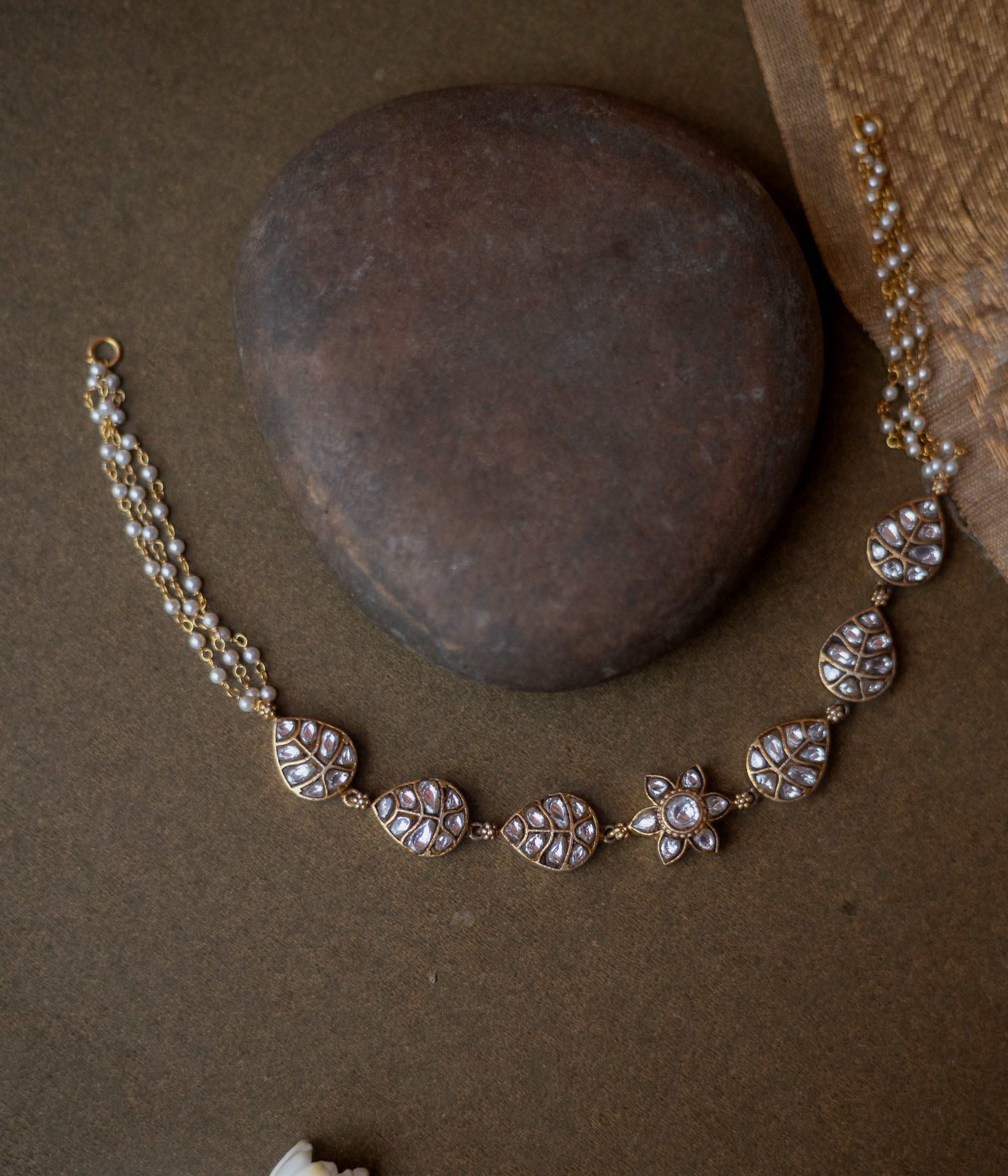 Gold choker with white kundan leaf motifs, floral centerpiece, and pearl chain detailing.