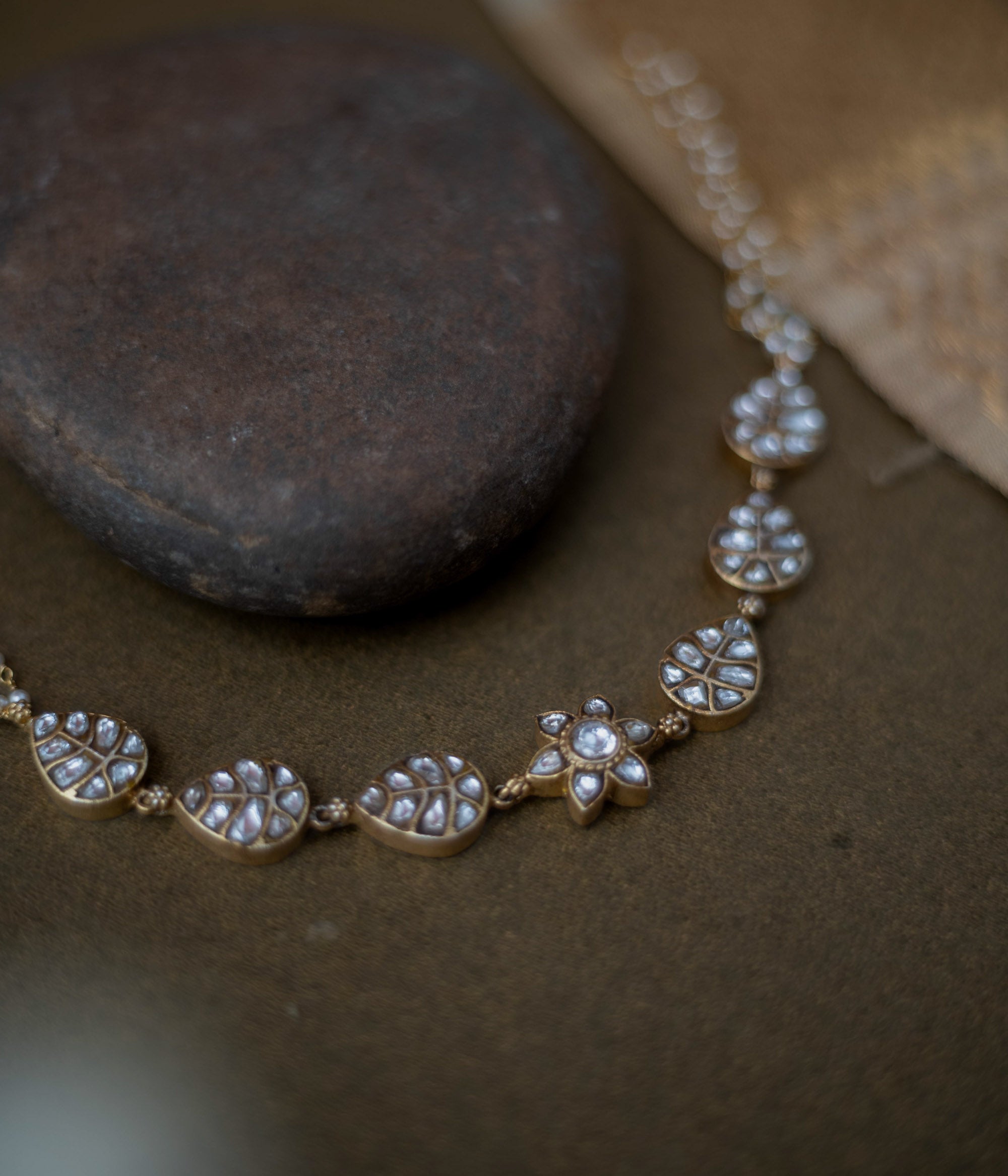 Gold choker with white kundan leaf motifs, floral centerpiece, and pearl chain detailing.