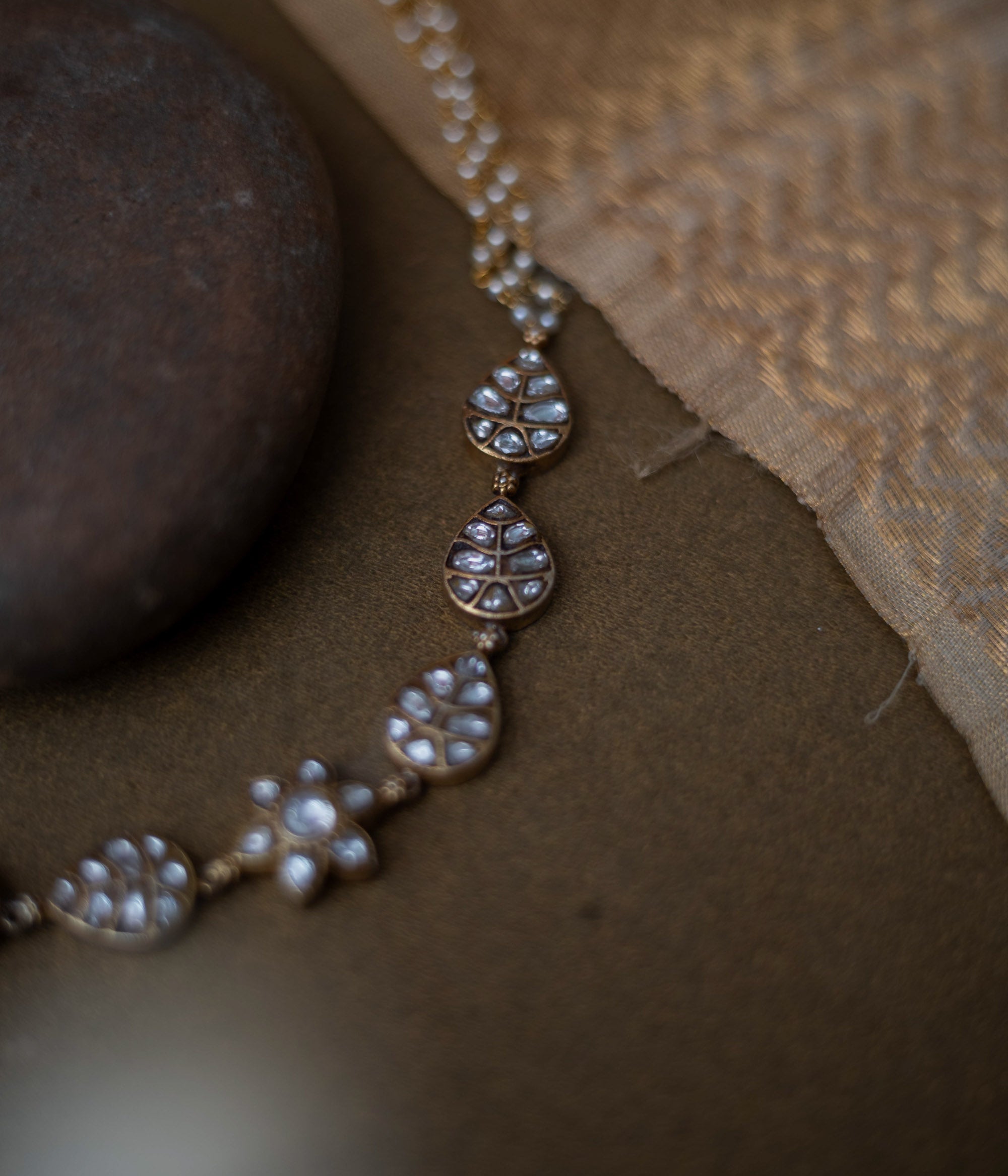 Gold choker with white kundan leaf motifs, floral centerpiece, and pearl chain detailing.