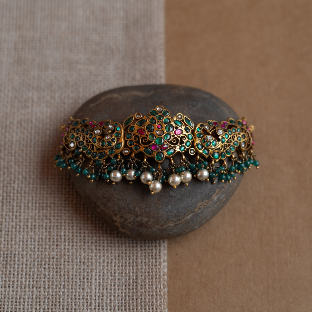 Peacock motif kundan choker with red, green, and white stones, green beads, and pearls.