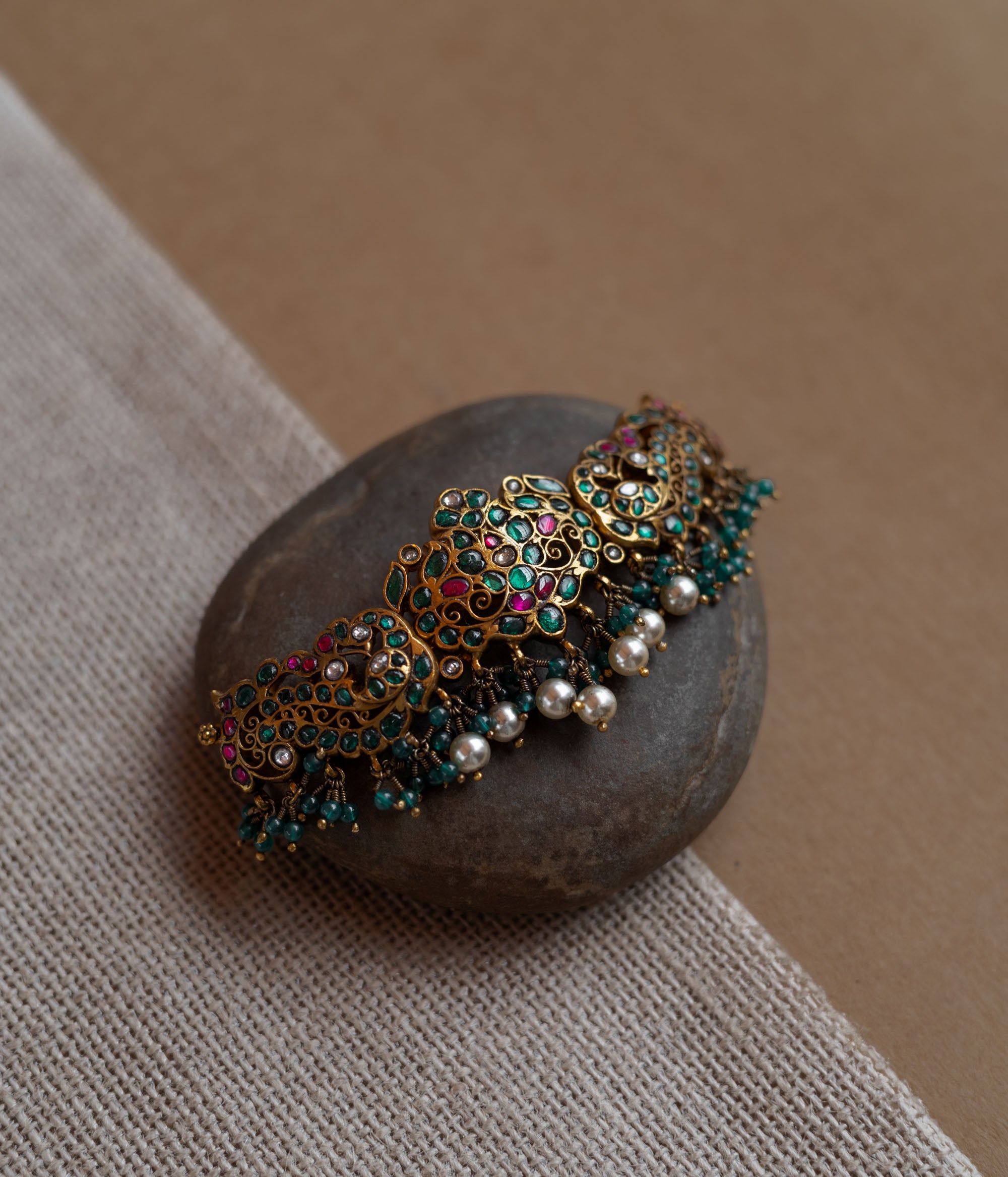 Peacock motif kundan choker with red, green, and white stones, green beads, and pearls.