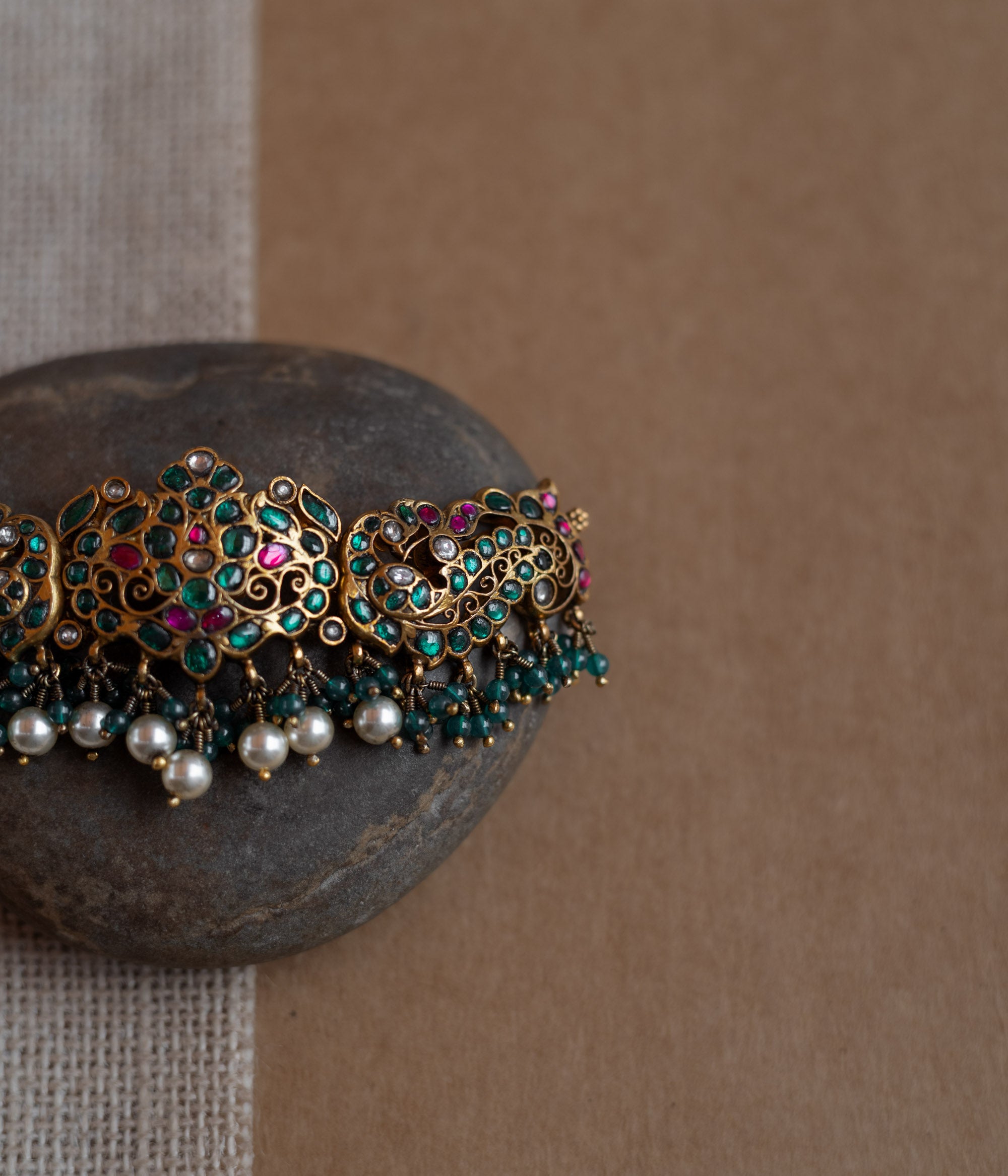 Peacock motif kundan choker with red, green, and white stones, green beads, and pearls.