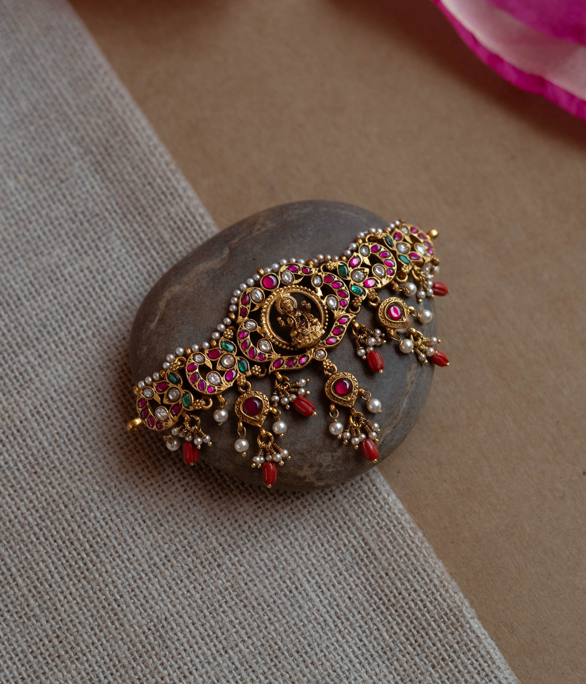 Intricate Kundan choker with a central deity. Features red, green, and white stones, red beads, and pearls.