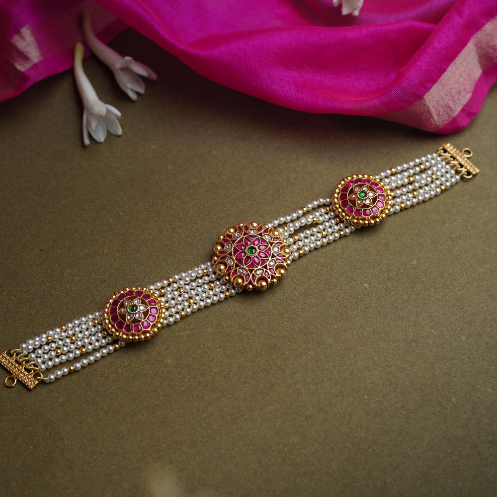 A multi-strand pearl choker featuring three circular, ornate gold Kundan medallions. Each medallion is set with red, green, and white Kundan stones.