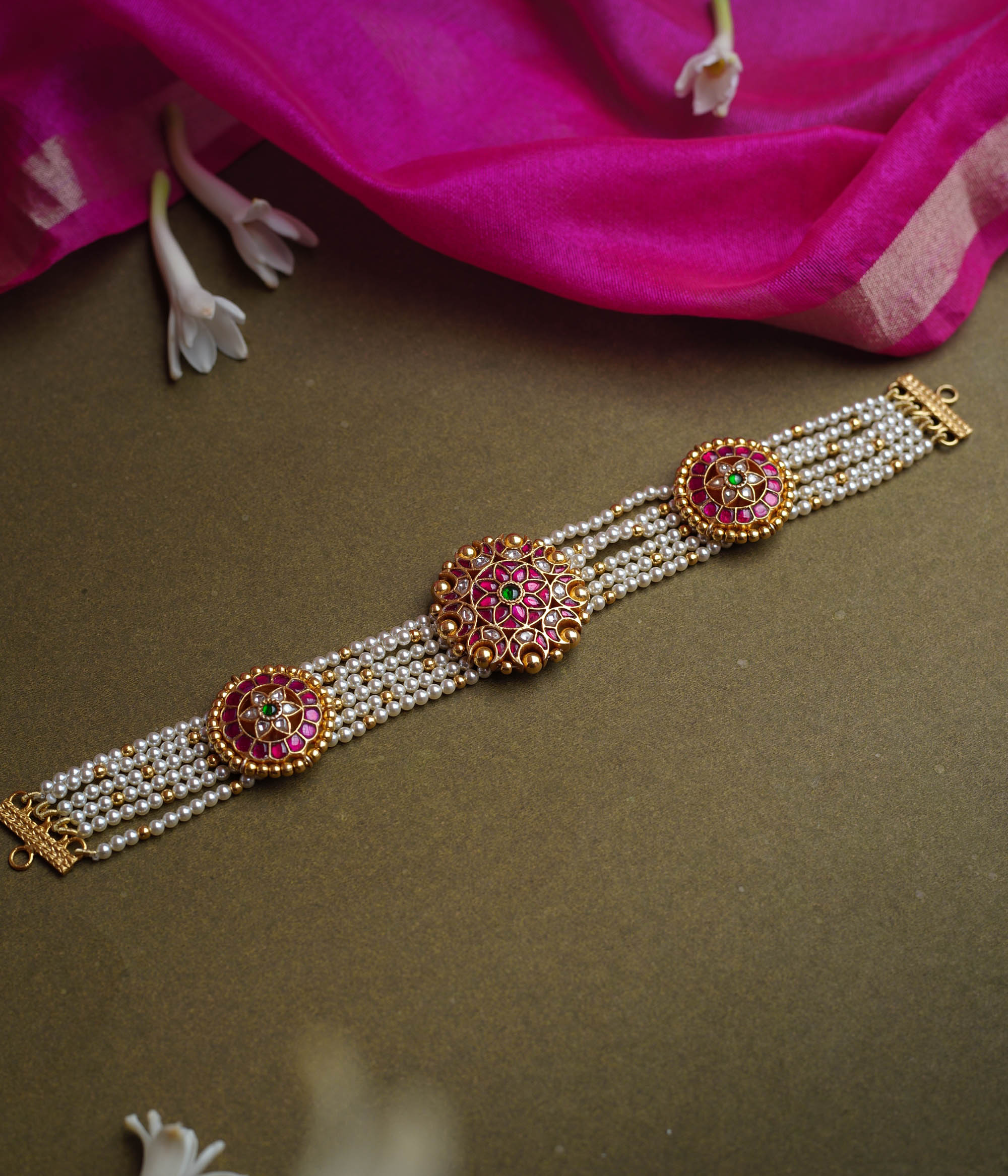 A multi-strand pearl choker featuring three circular, ornate gold Kundan medallions. Each medallion is set with red, green, and white Kundan stones.