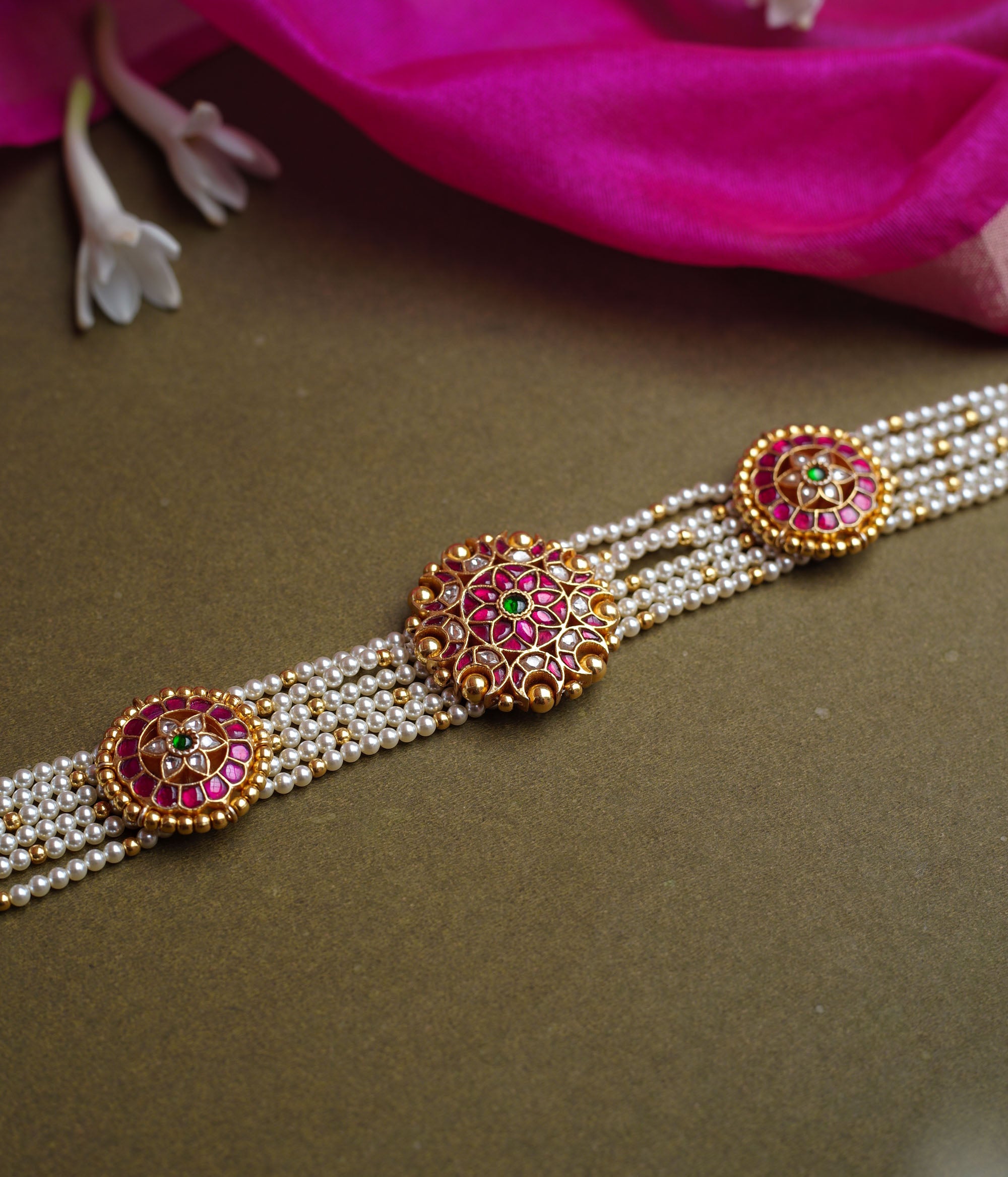 A multi-strand pearl choker featuring three circular, ornate gold Kundan medallions. Each medallion is set with red, green, and white Kundan stones.