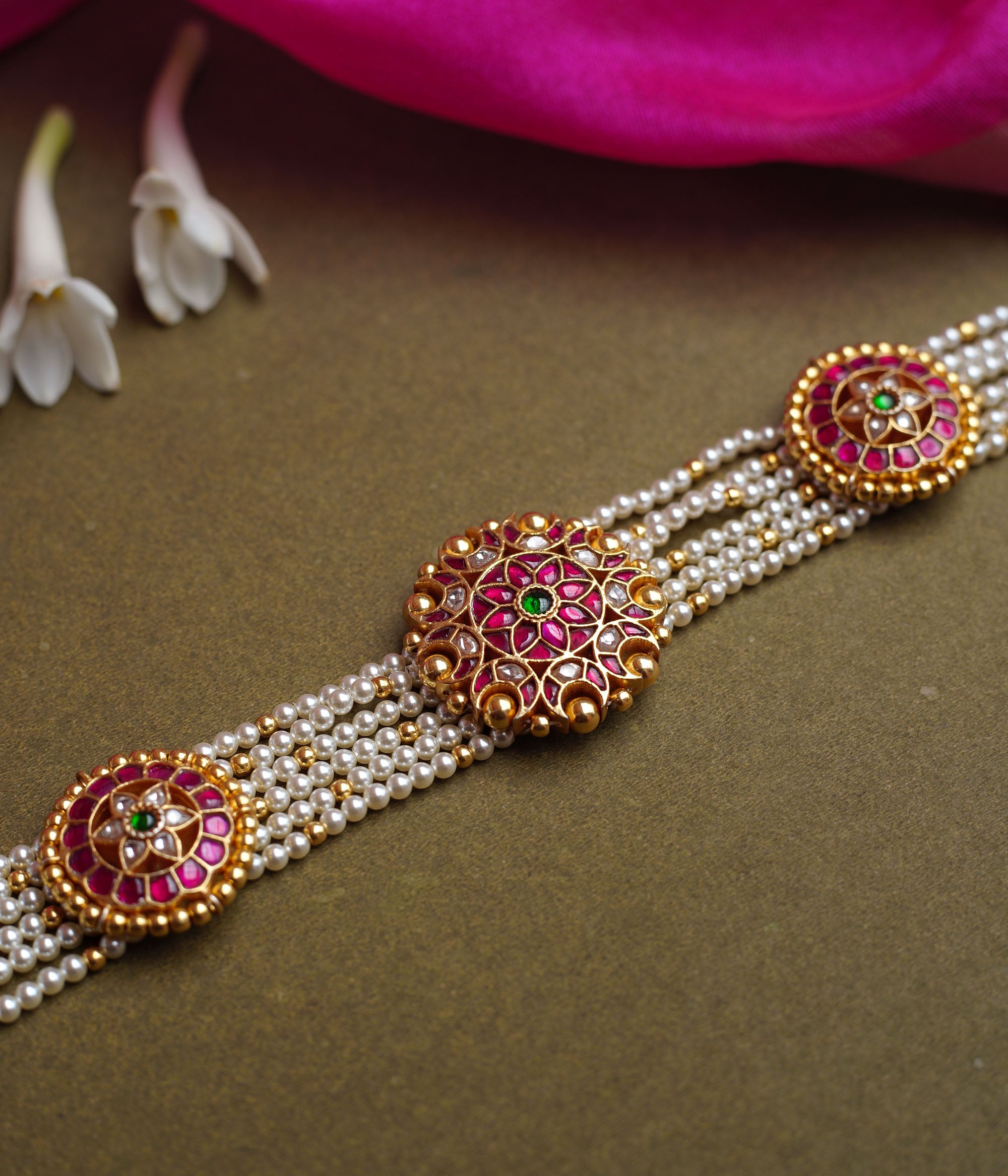 A multi-strand pearl choker featuring three circular, ornate gold Kundan medallions. Each medallion is set with red, green, and white Kundan stones.