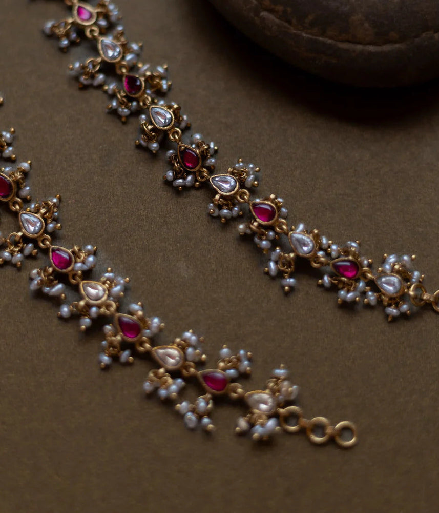 Delicate gold necklace with red and white stones on a brown surface