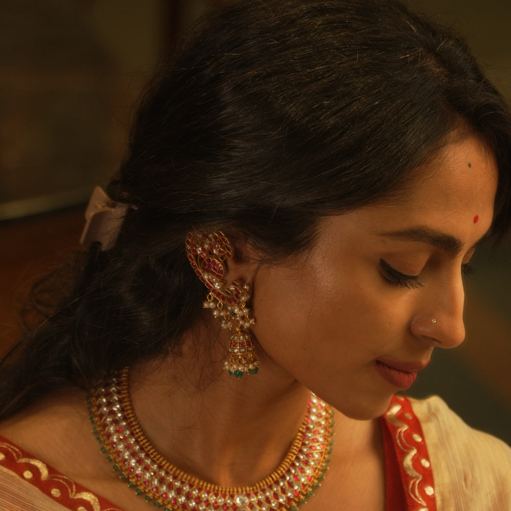Peacock-inspired kundan earrings with red, green, and white stones, featuring pearl and bead hangings.
