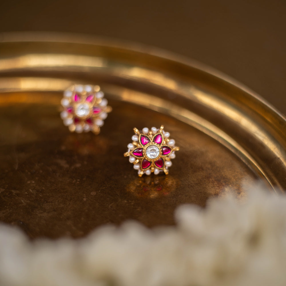 Meira Kundan Earrings with red and white kundan stones and pearl accents on a floral base, placed on a golden brass surface.