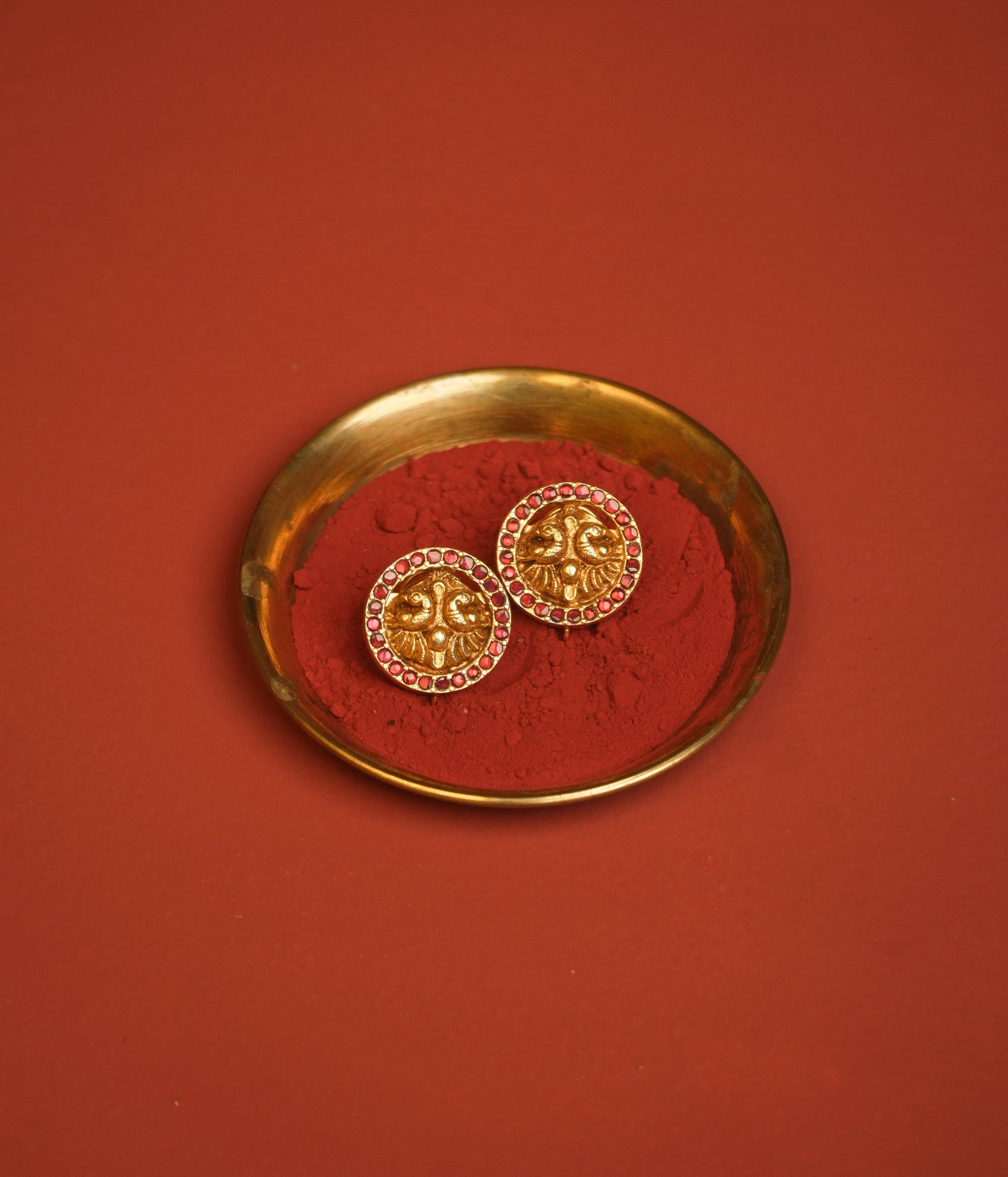 Gold earrings on a red powder with a gold dish against a red background
