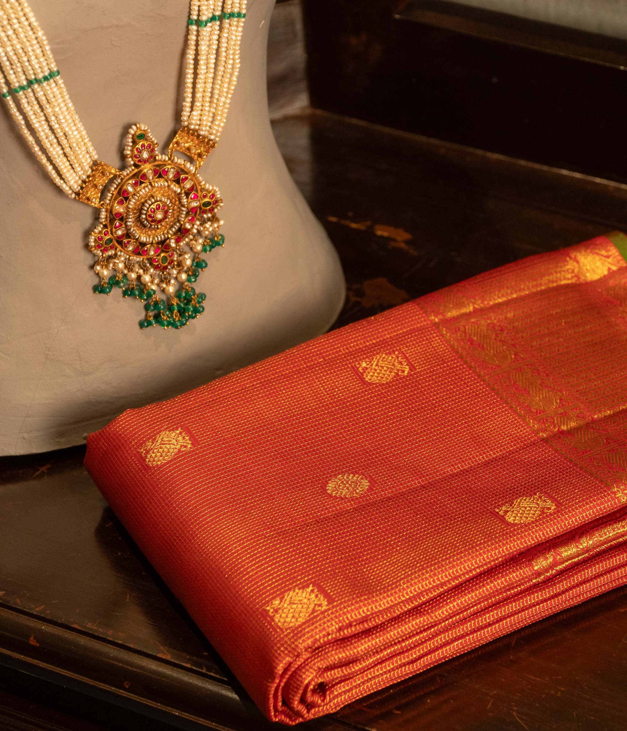 Pearl-string Kundan necklace with circular pendant, red and green stones, and green bead hangings.
