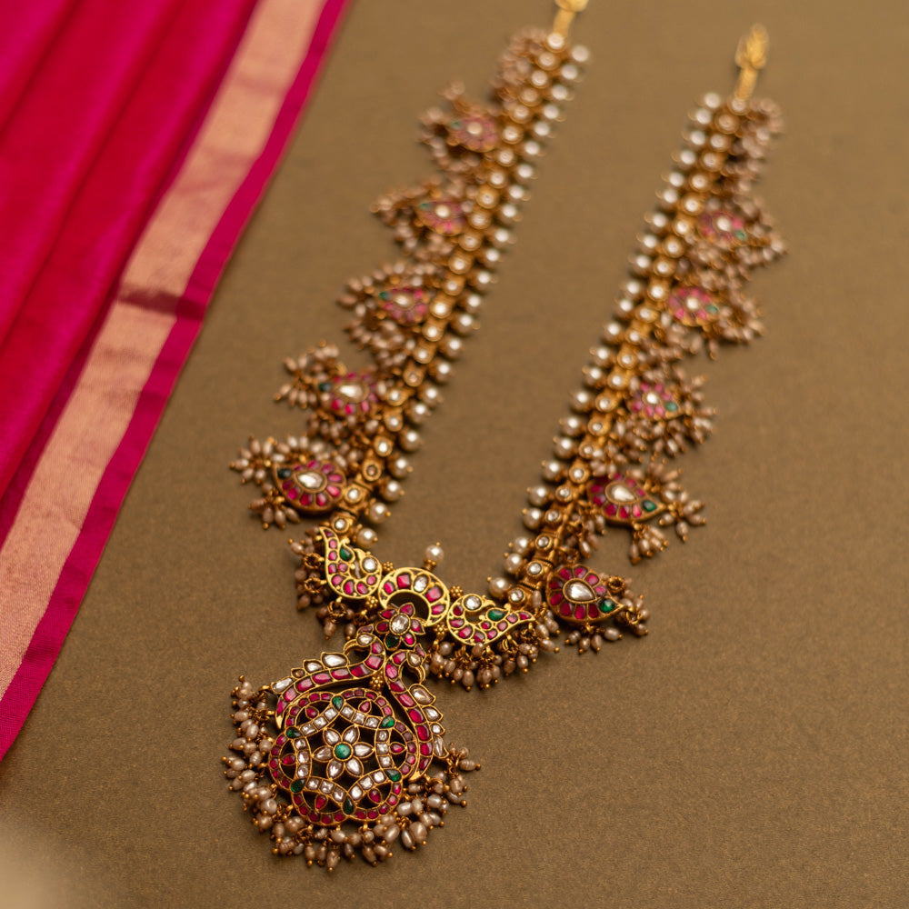 Overhead view of a Gutta Pusalu necklace with pearls and colored stones. The necklace rests on a brown surface with a pink fabric accent.
