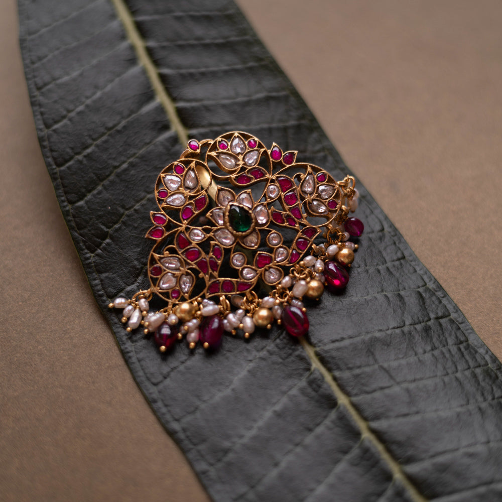 Lotus-inspired kundan pendant with red, green, and white stones, pearls, and dangling red beads.