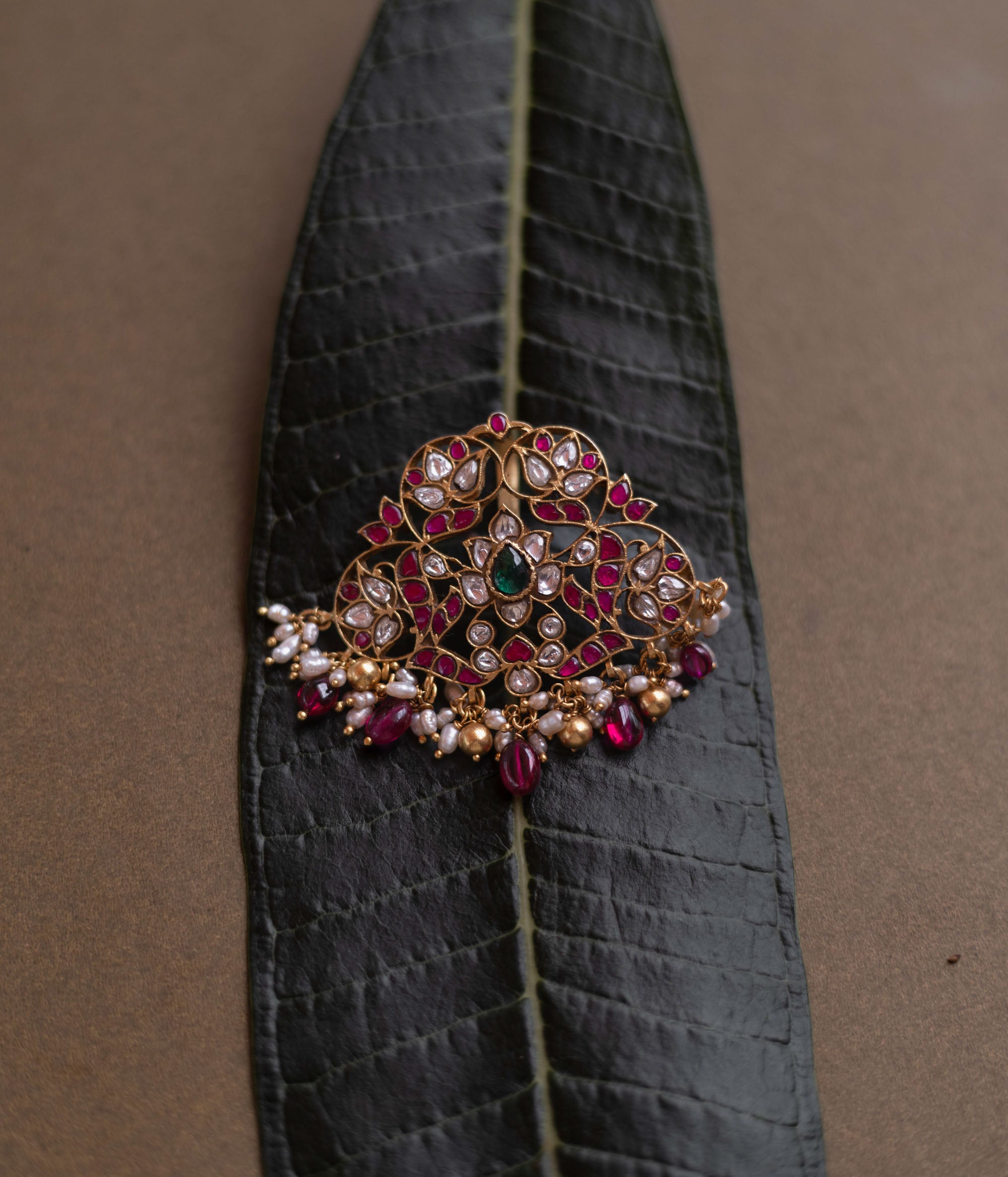 Lotus-inspired kundan pendant with red, green, and white stones, pearls, and dangling red beads.