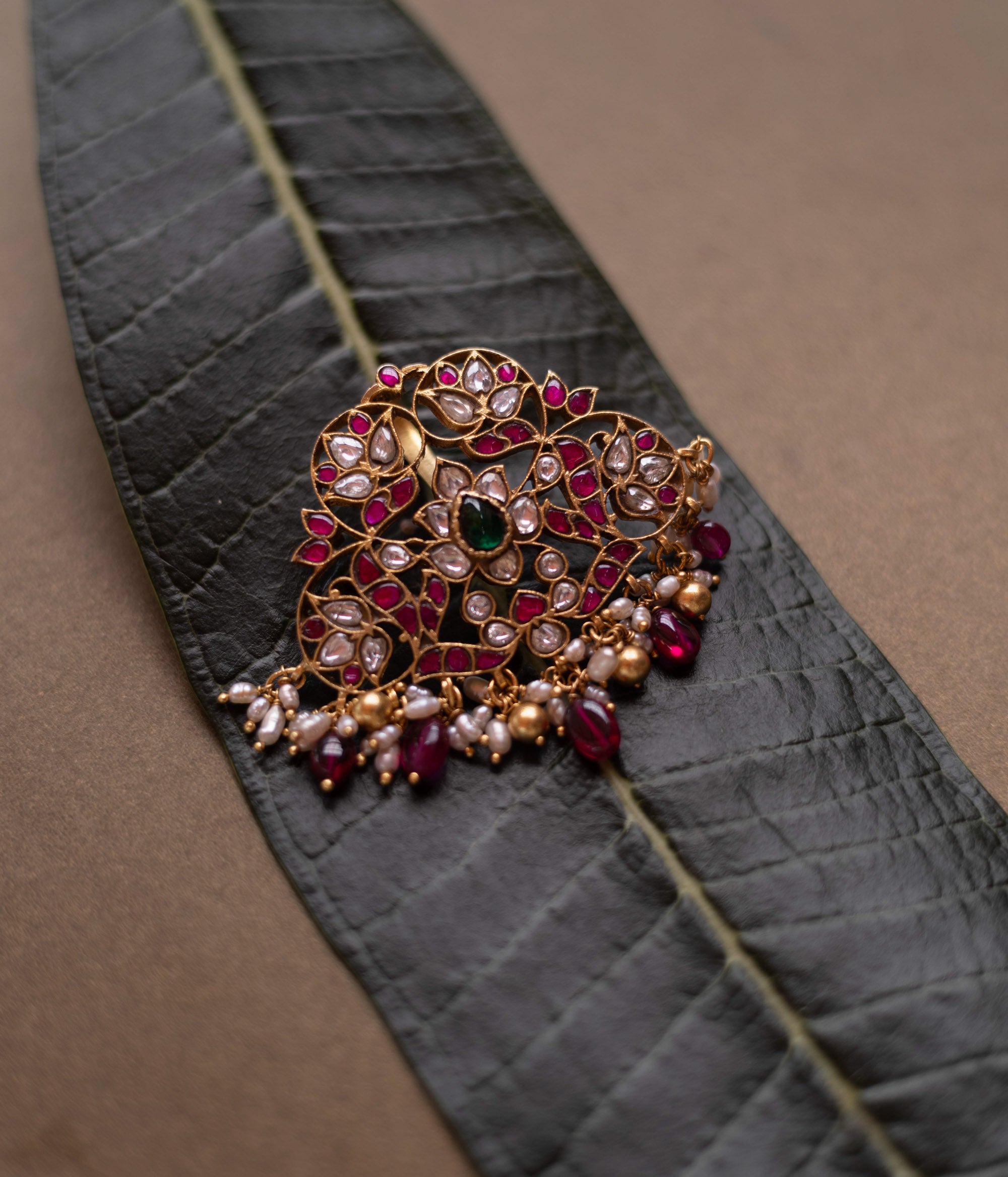 Lotus-inspired kundan pendant with red, green, and white stones, pearls, and dangling red beads.