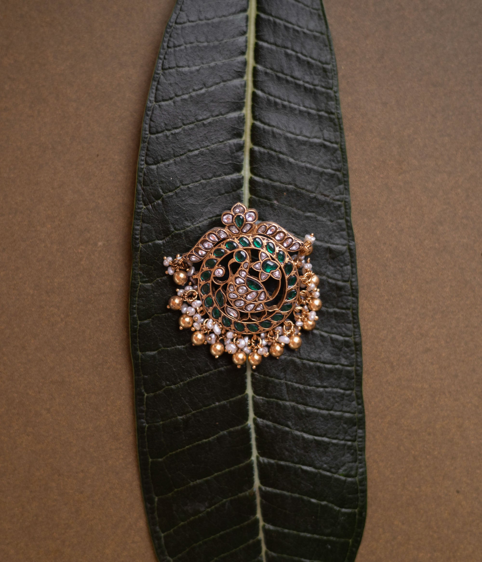 Circular kundan pendant featuring twin peacocks with green and white stones and pearl fringe.