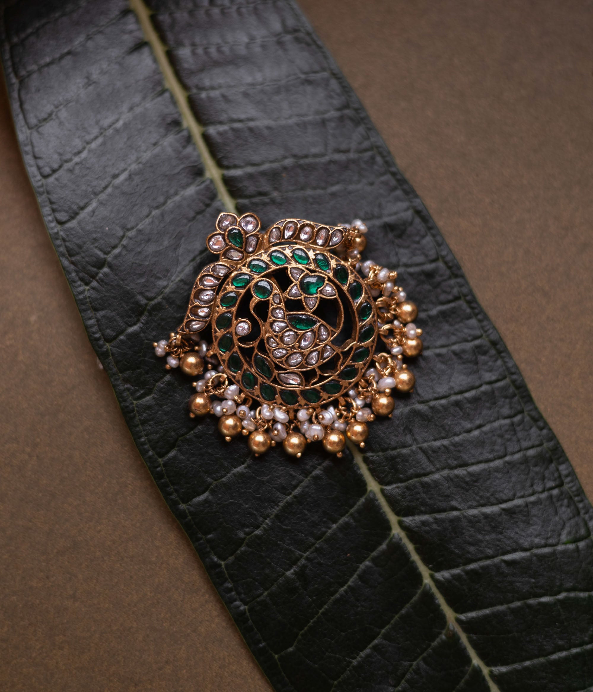 Circular kundan pendant featuring twin peacocks with green and white stones and pearl fringe.