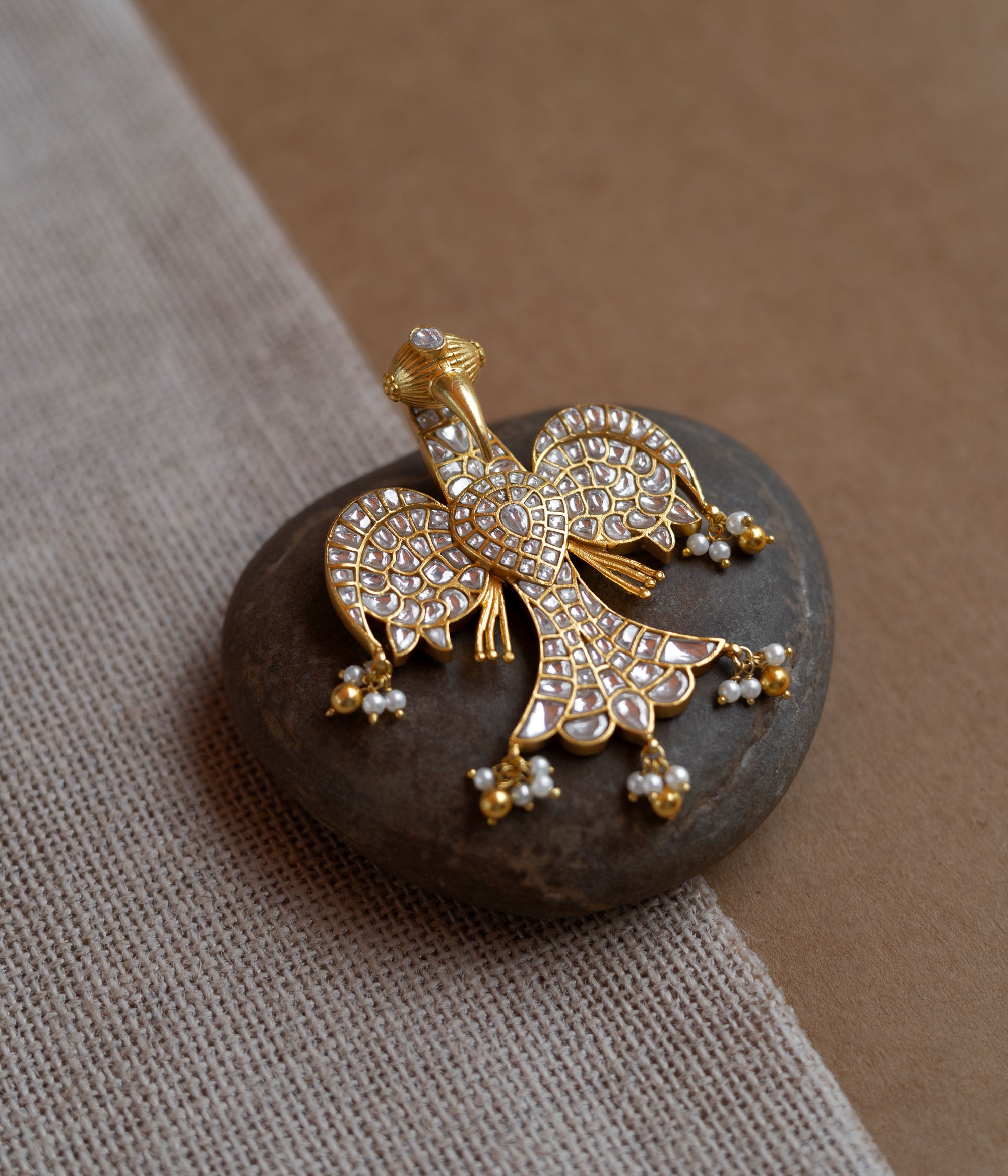 Peacock-shaped kundan pendant with white stones and pearl hangings in a traditional gold design.