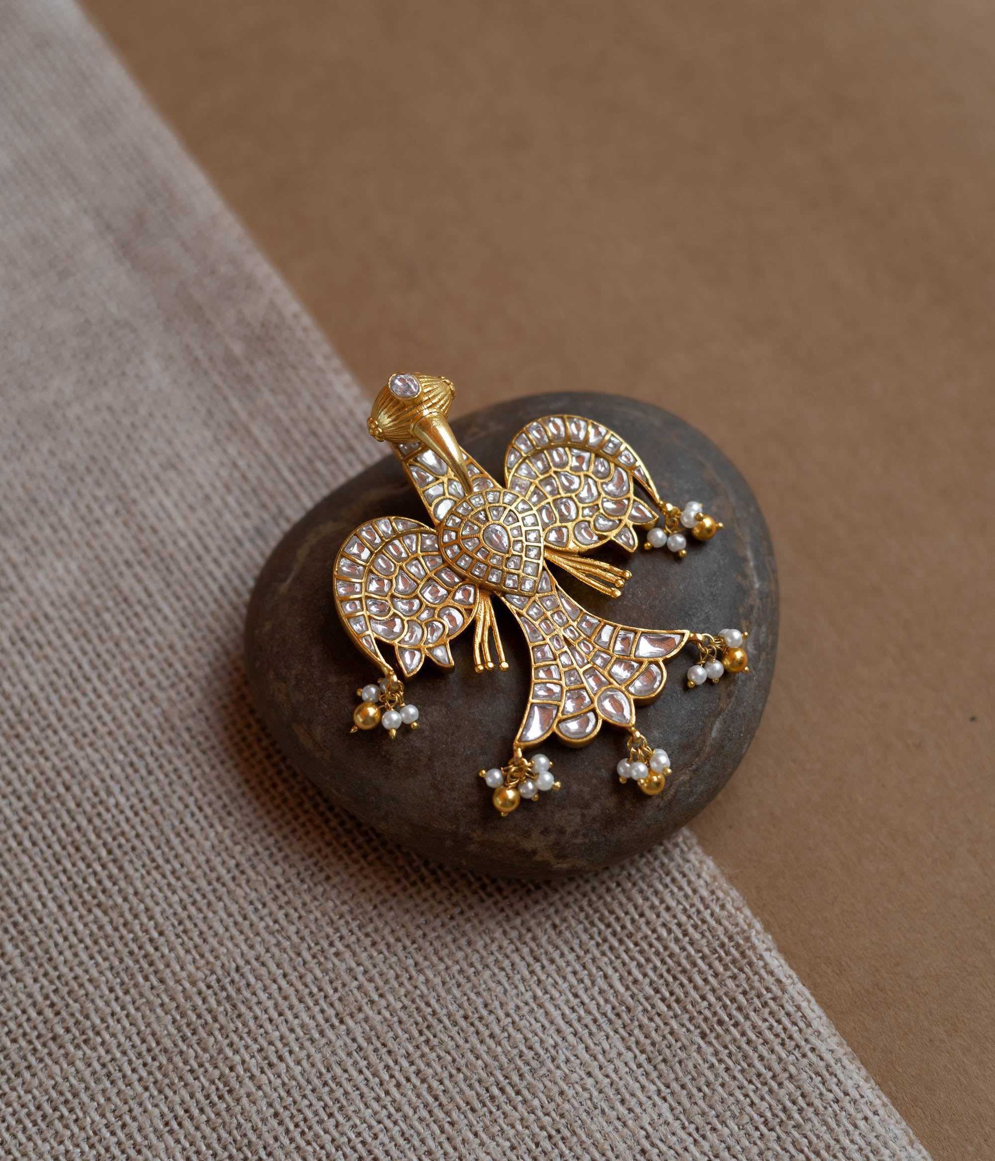 Peacock-shaped kundan pendant with white stones and pearl hangings in a traditional gold design.