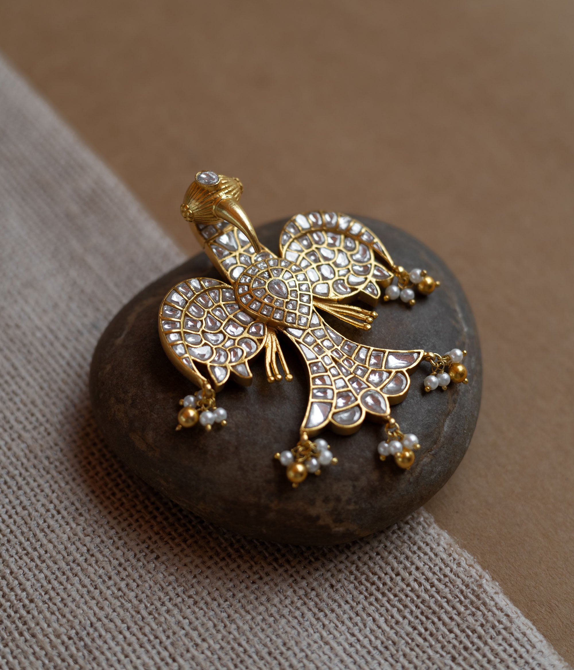 Peacock-shaped kundan pendant with white stones and pearl hangings in a traditional gold design.
