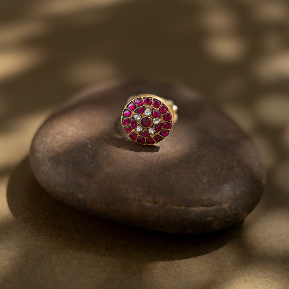 Close-up of the Karisa Divya Ring. Features red moissanite and white stones in a Polki setting, resting on a smooth, dark stone.