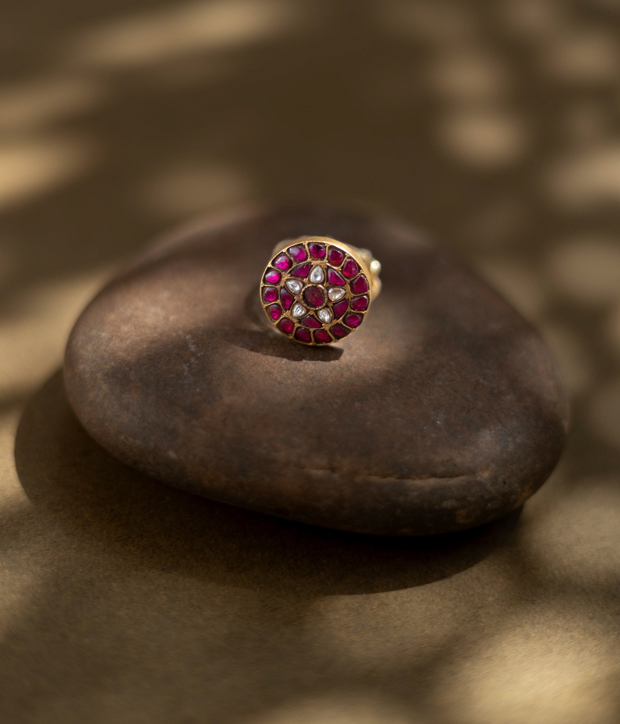 Close-up of the Karisa Divya Ring. Features red moissanite and white stones in a Polki setting, resting on a smooth, dark stone.