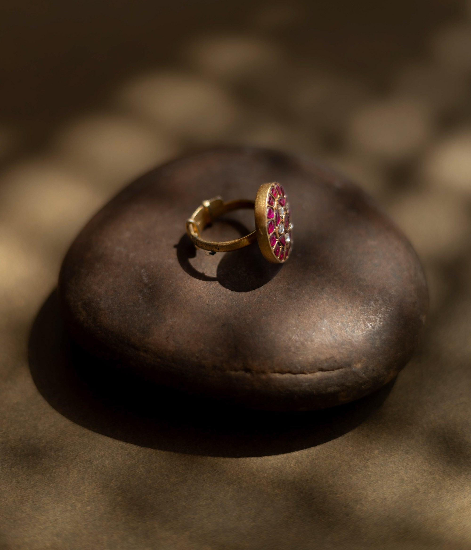 Close-up of the Karisa Divya Ring. Features red moissanite and white stones in a Polki setting, resting on a smooth, dark stone.
