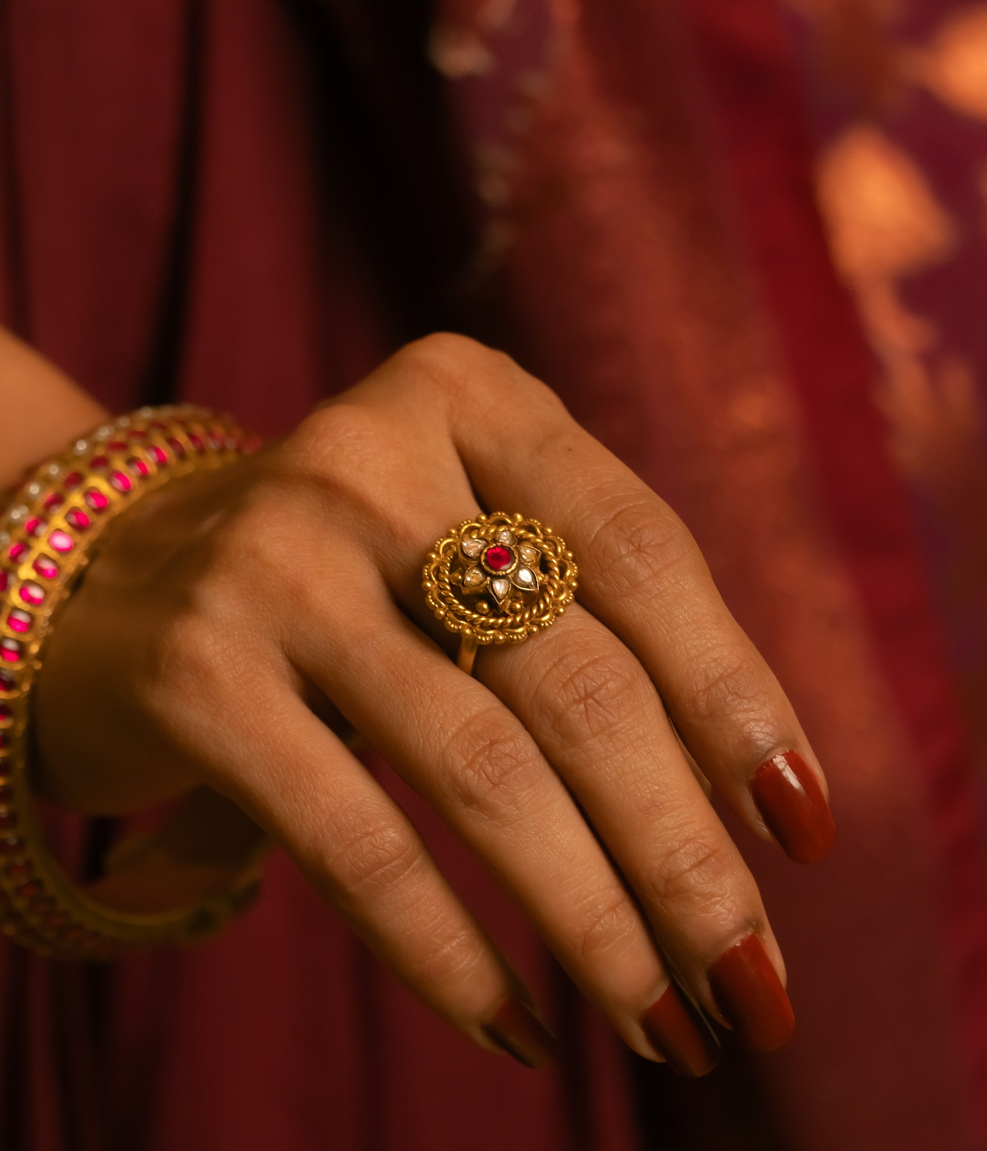 Gold floral ring with red and white Kundan stones, worn with matching bangle on hand.