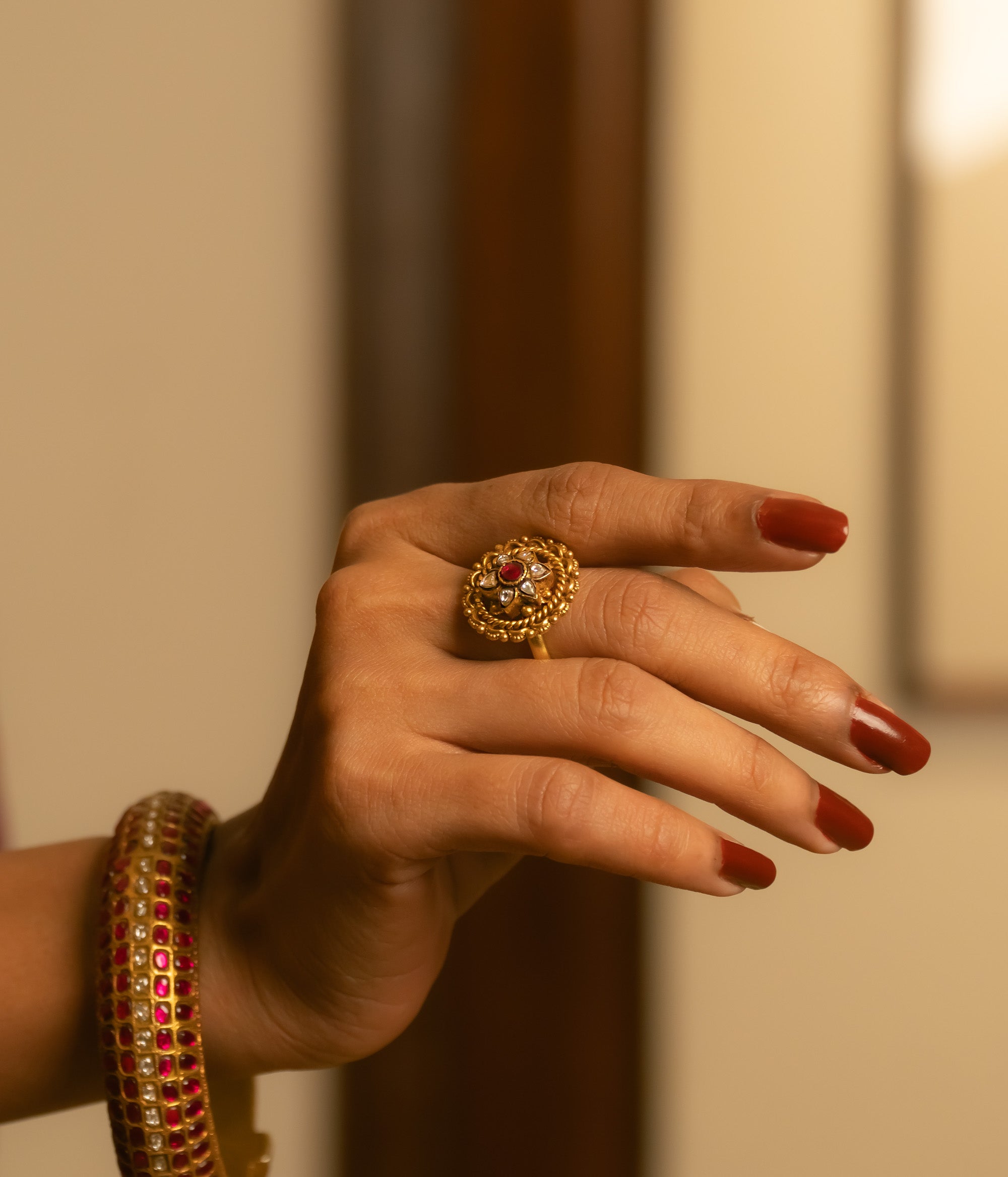 Gold floral ring with red and white Kundan stones, worn with matching bangle on hand.