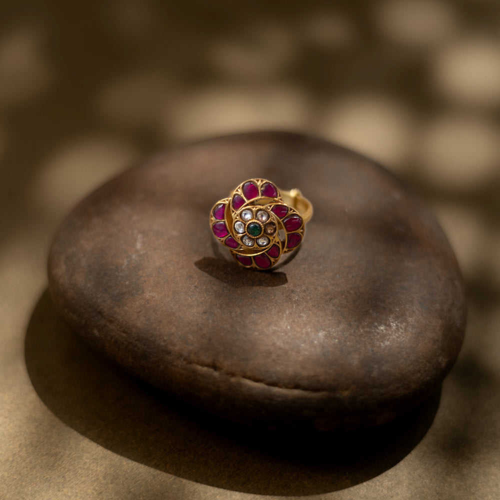 Detailed view of a golden ring. Magenta, ruby, and green stones form a floral design in Kundan style.
