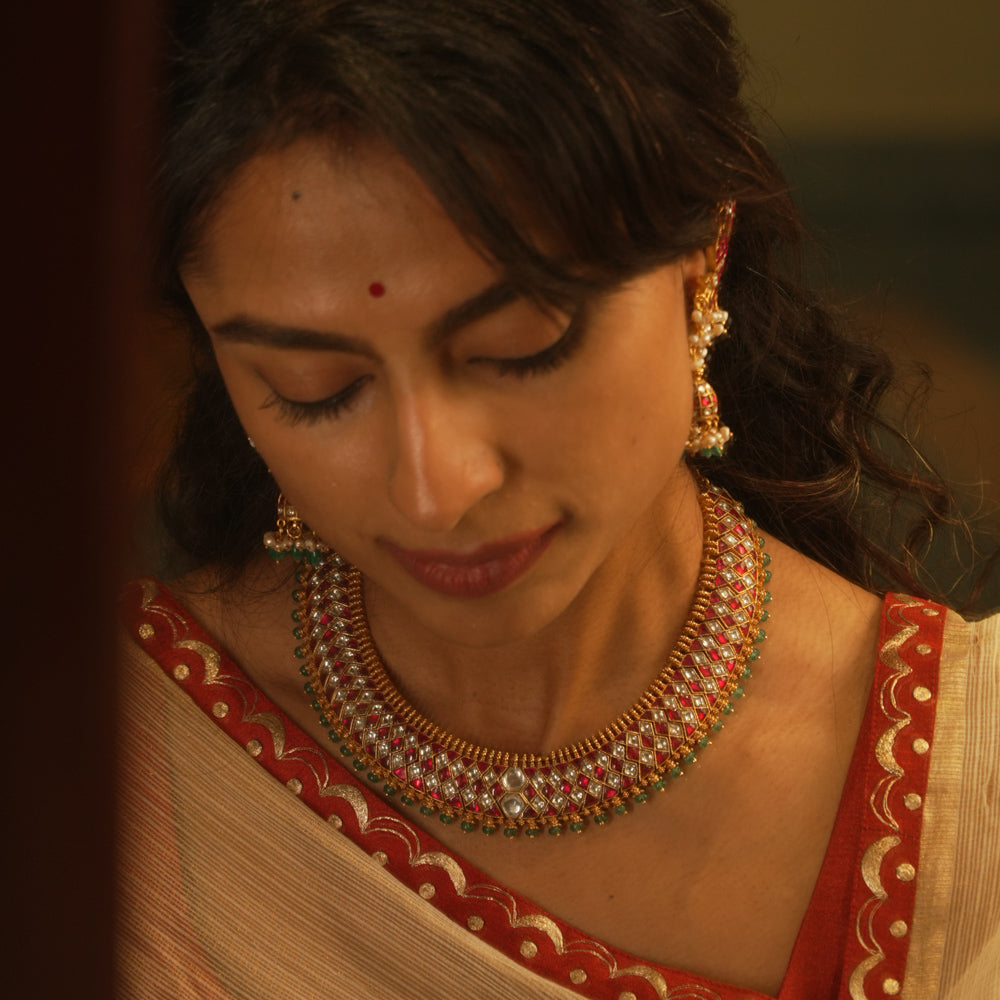 Gold Kundan necklace with red and white kundan stones, and green beads, on a woman's neck.
